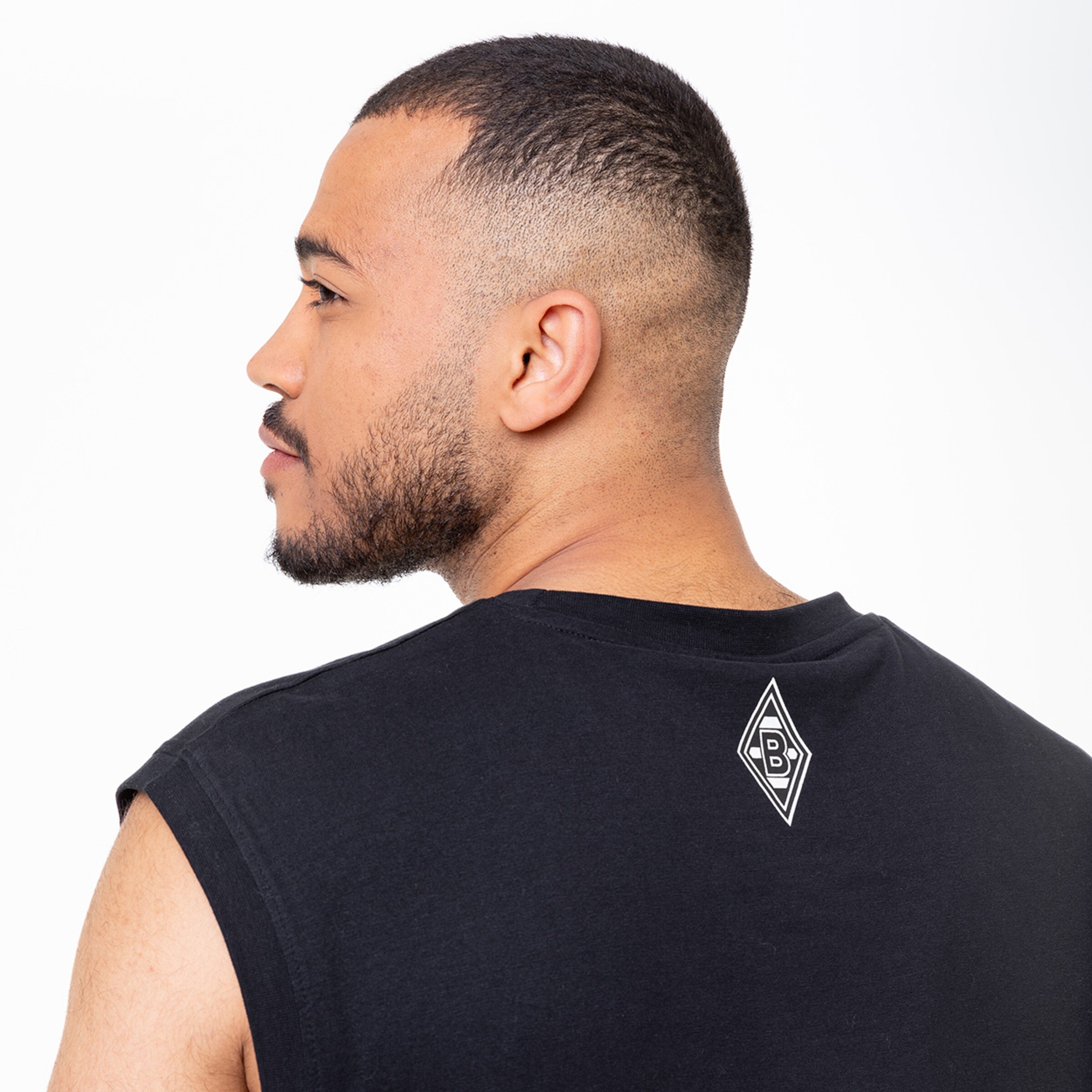 Mann mit Kurzhaarschnitt trägt ein ärmelloses schwarzes Shirt mit Borussia Mönchengladbach Logo.