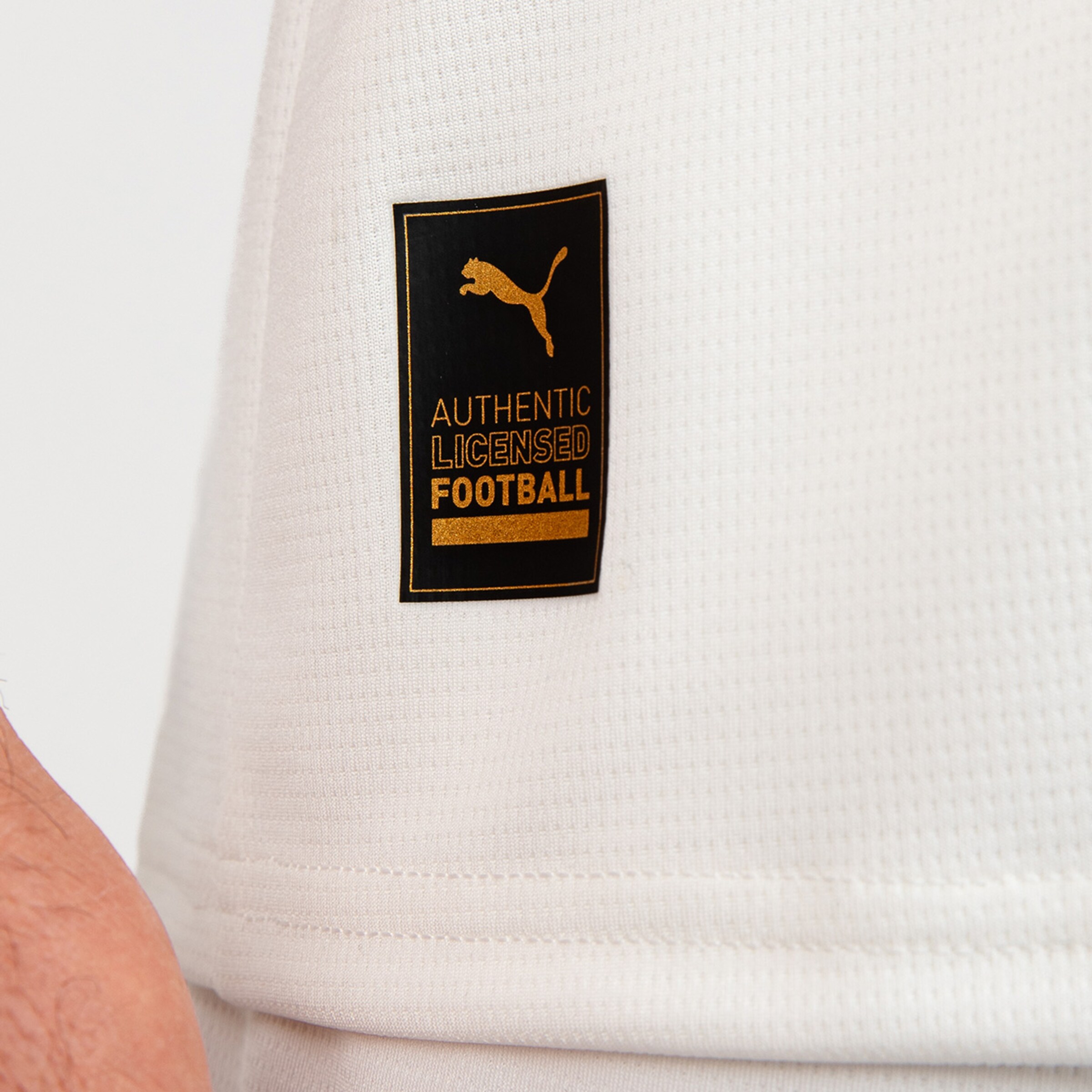 Label mit dem Text AUTHENTIC LICENSED FOOTBALL von Puma auf einem weißen Trikot.