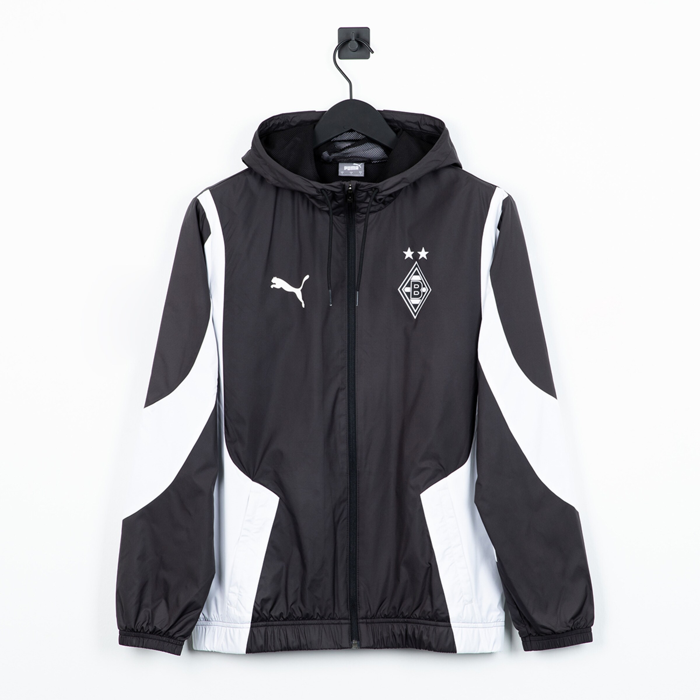 Schwarze Puma Borussia Mönchengladbach Windjacke mit weißen Einsätzen und Kapuze, hängend auf einem schwarzen Kleiderbügel vor weißer Wand.