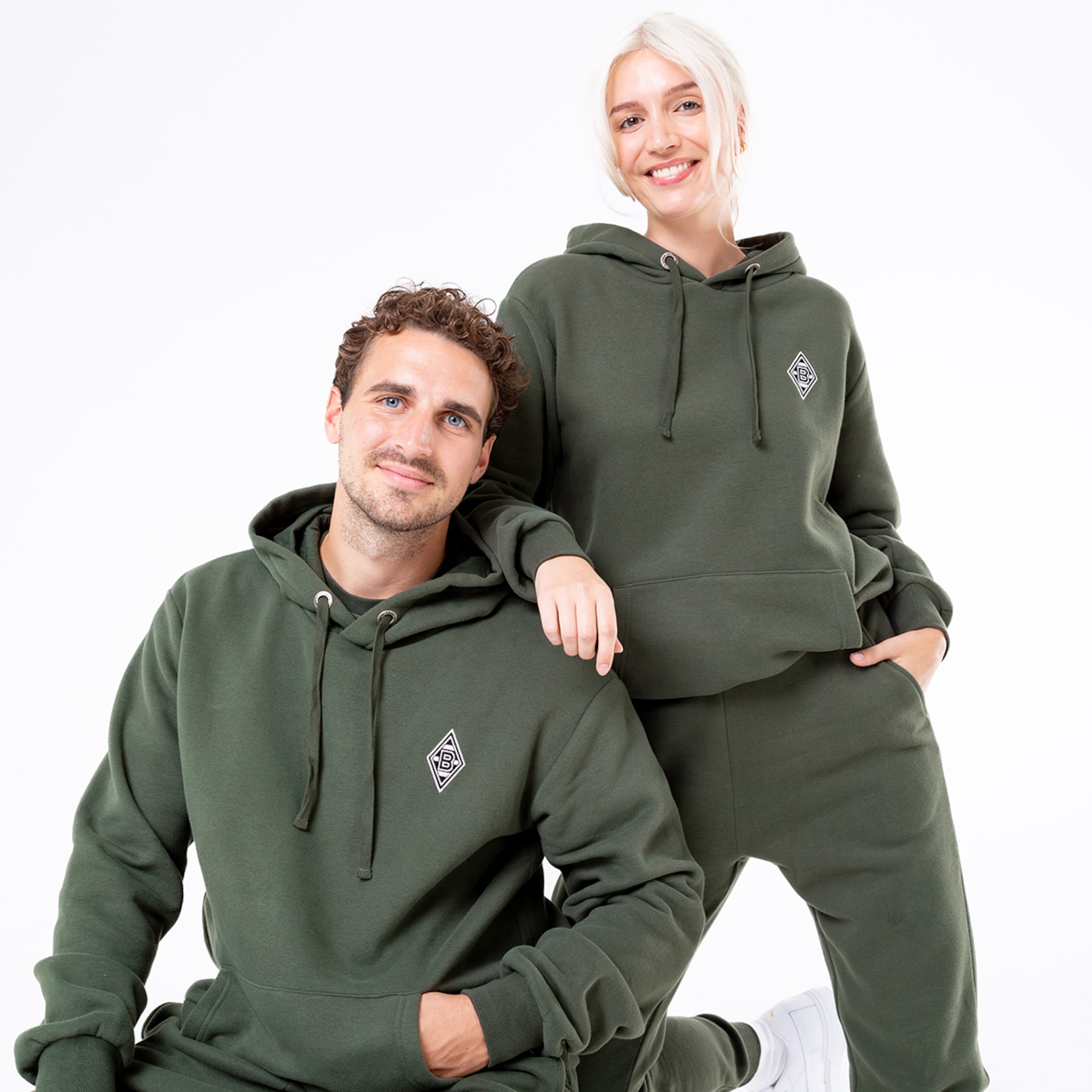 Paar in lässiger Sportbekleidung beide tragen grüne Hoodies mit Logo.