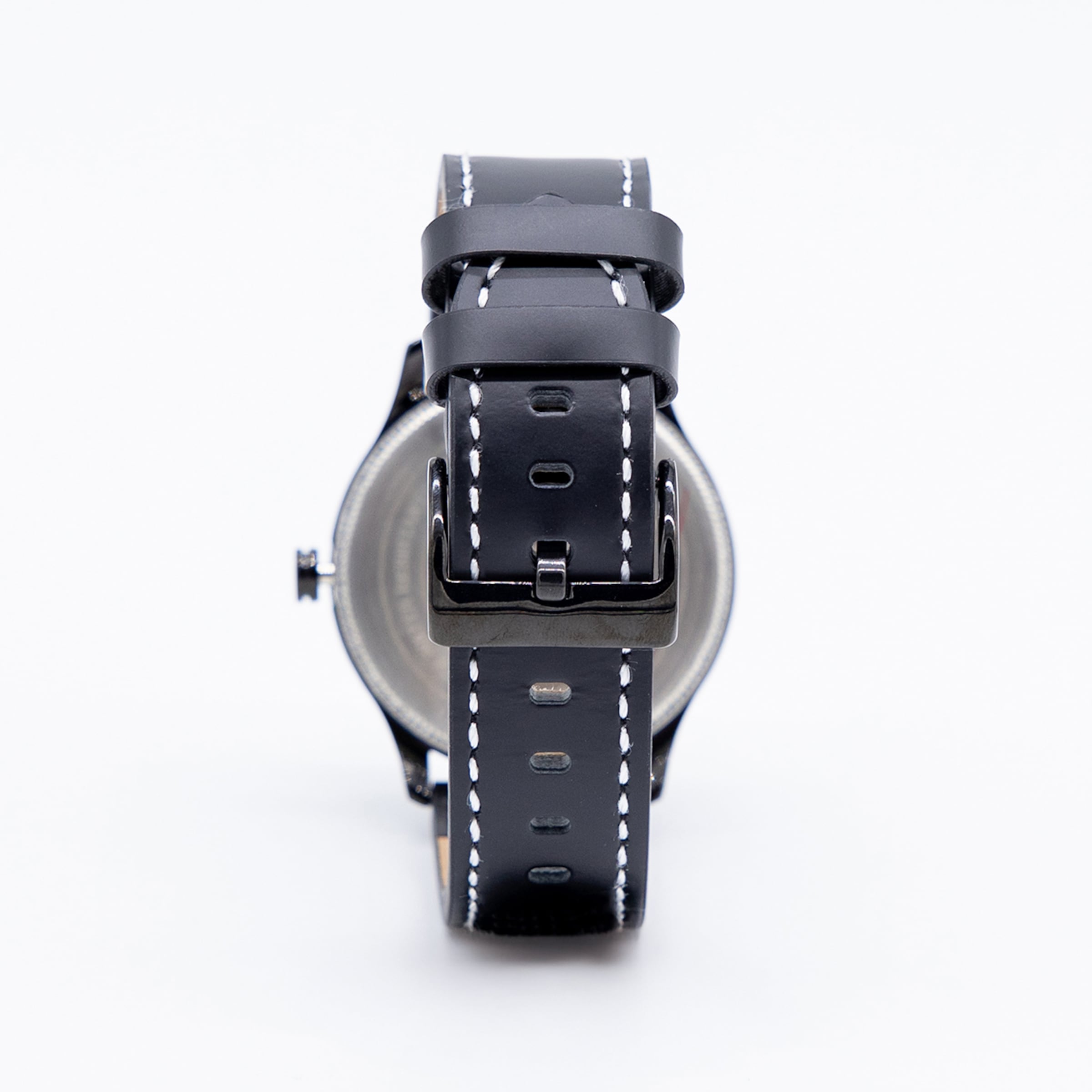 Rückansicht einer schwarzen Armbanduhr mit Lederarmband, weißen Ziernähten und schwarzer Dornschließe vor weißem Hintergrund.