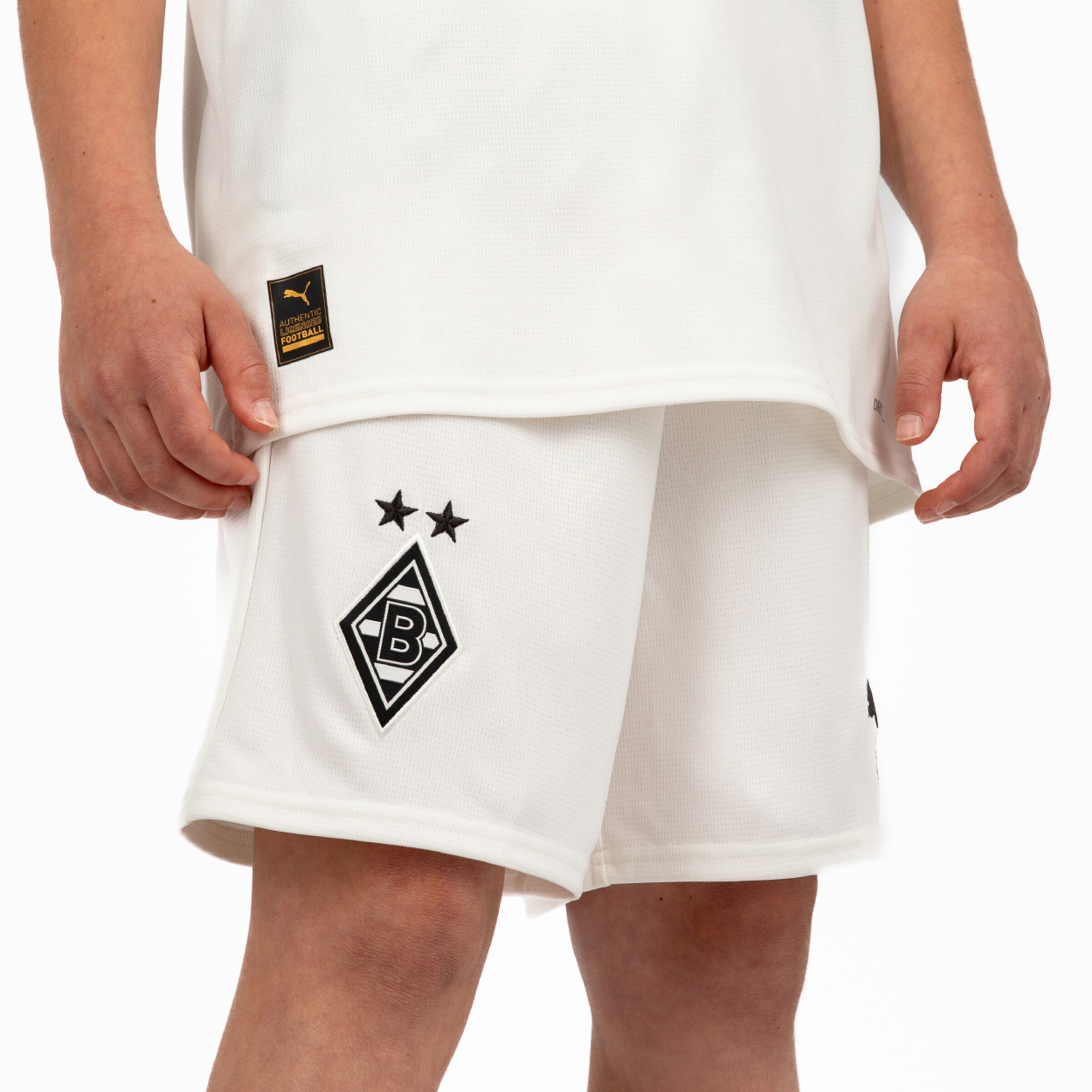 Ein Kind trägt eine weiße Borussia Mönchengladbach Fußballshorts mit einem schwarzen Vereinslogo.