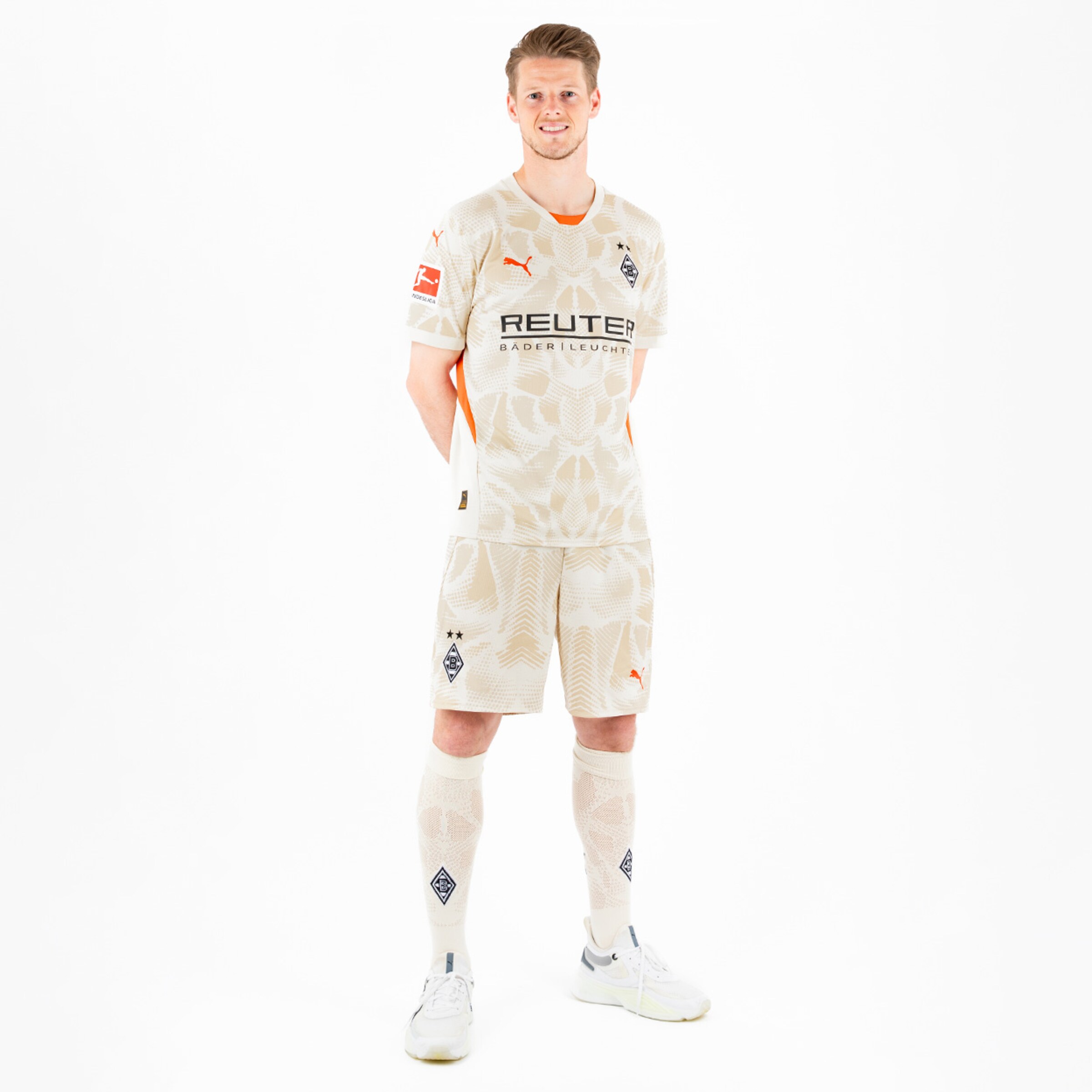 Spieler in einem beigen Fußballtrikots mit Puma-Logo lächelt.