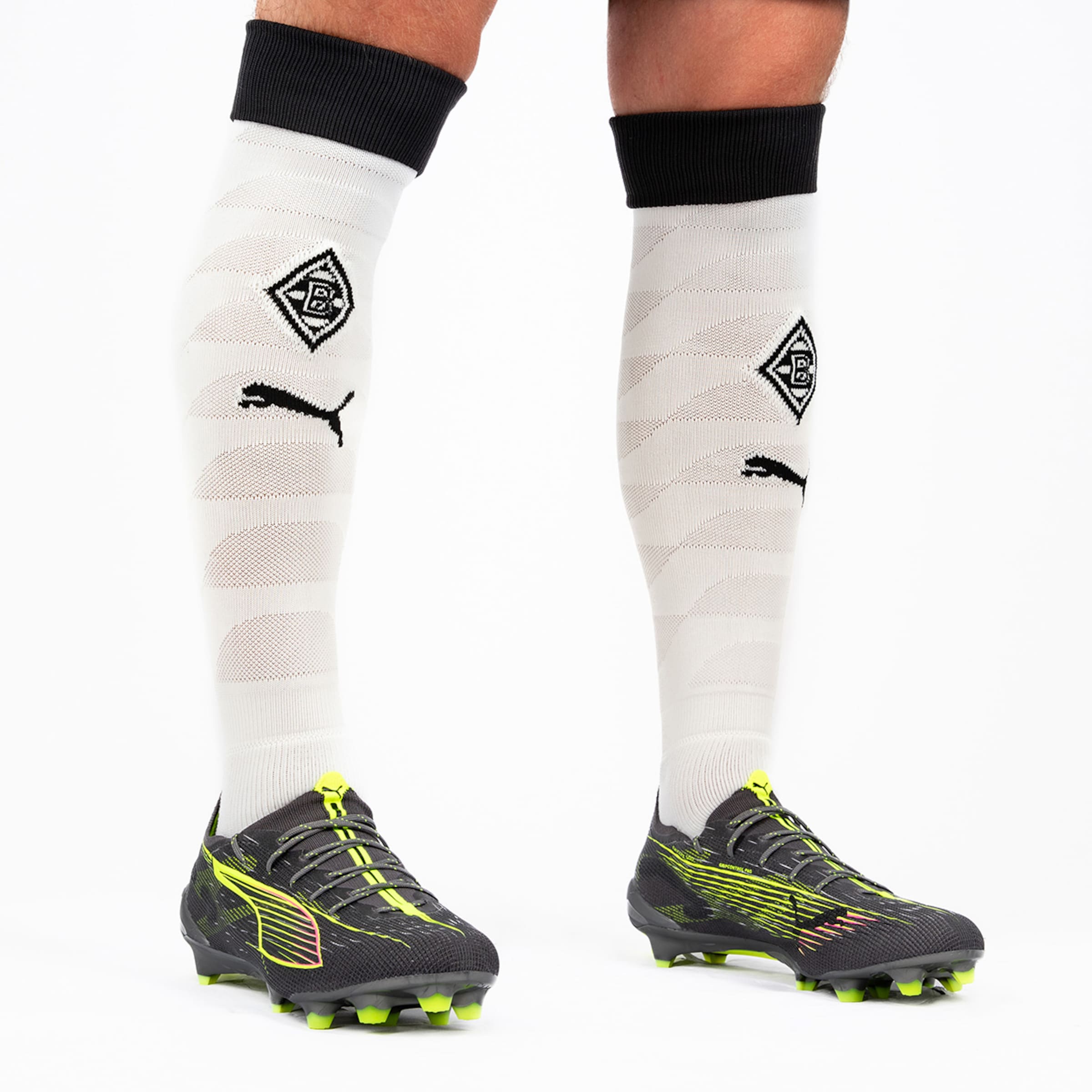 A player wears black soccer cleats and white socks featuring Borussia Mönchengladbach logo and Puma symbol.