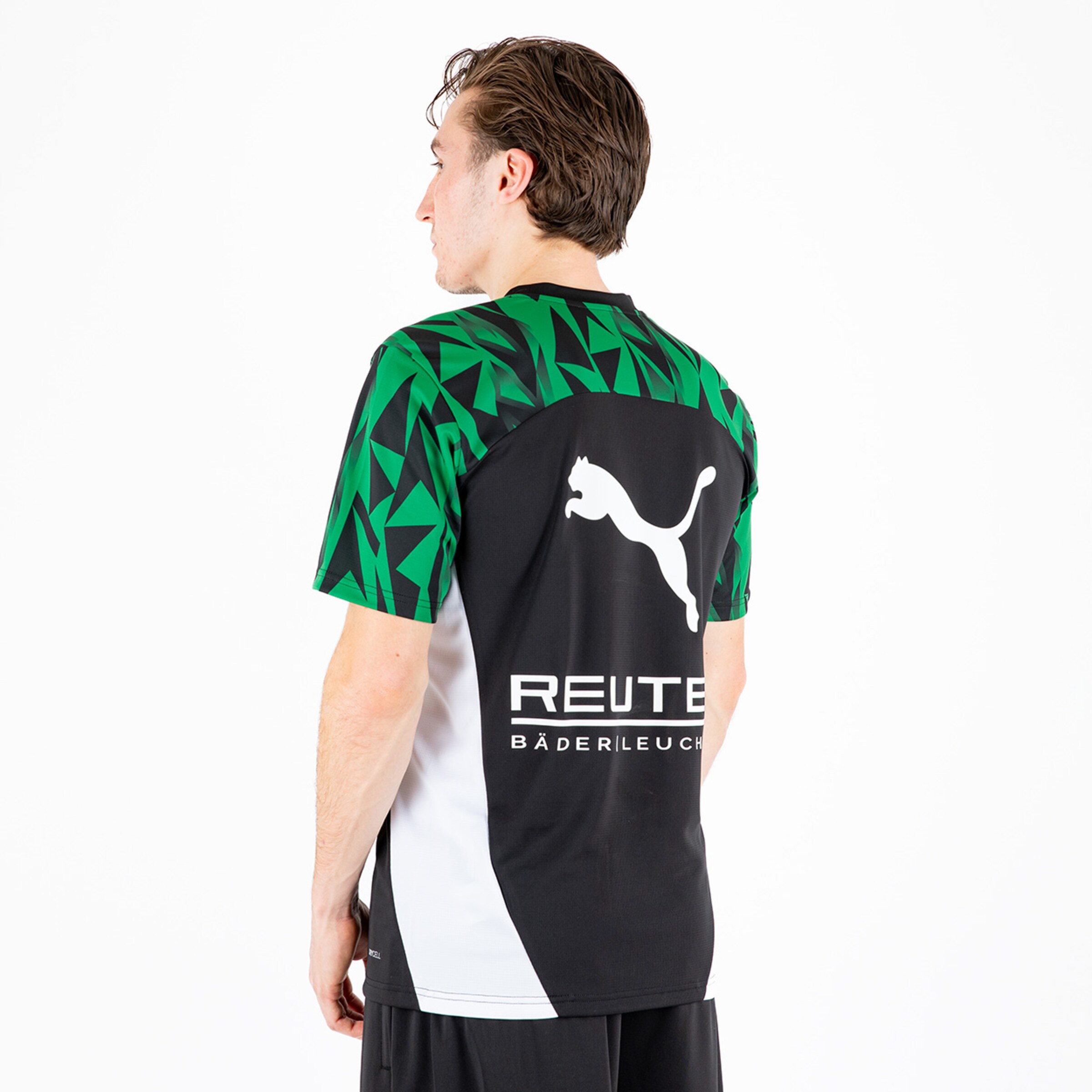 Ein Mann trägt ein Trikot mit dem Puma-Logo und einem geometrischen Muster in Grün und Schwarz.
