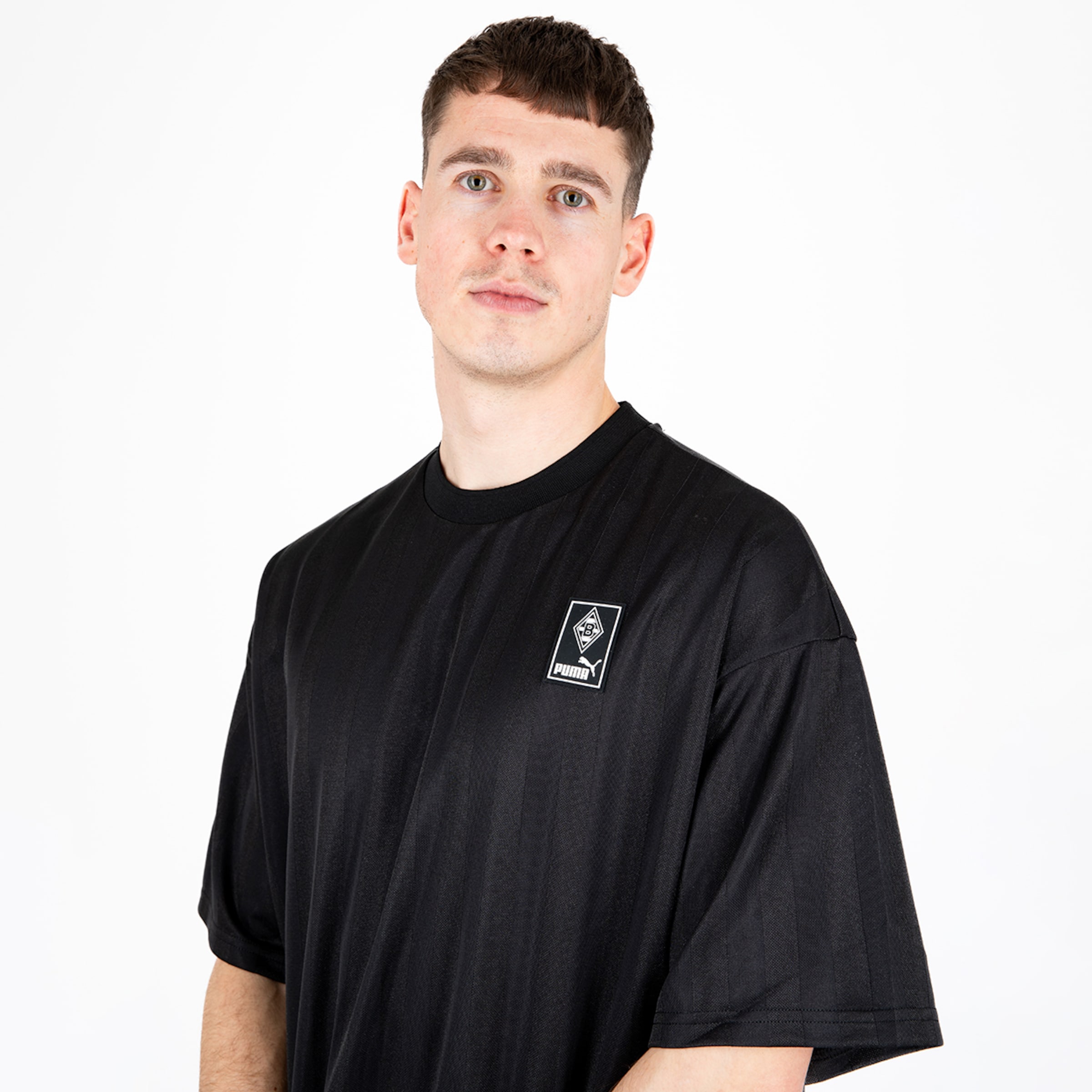 Junger Mann trägt ein schwarzes T-Shirt mit einem kleinen Vereinslogo.
