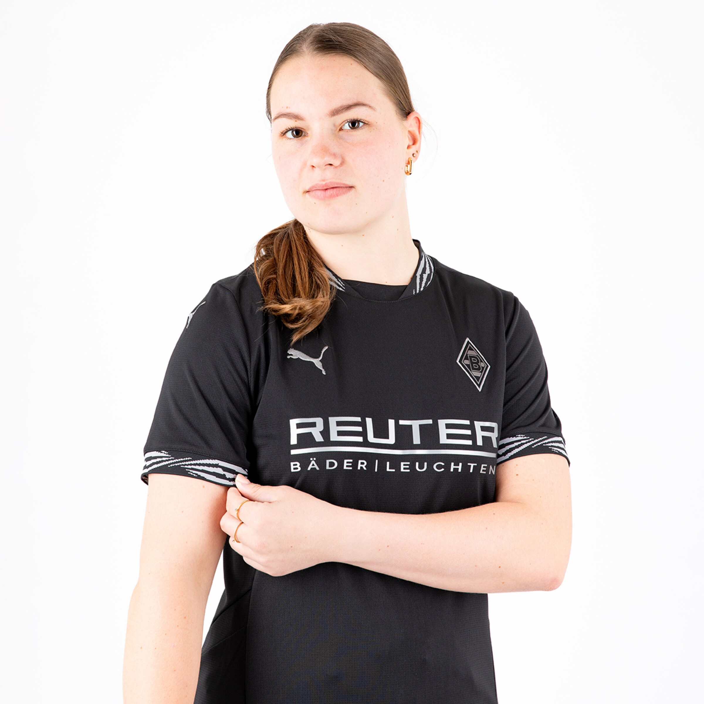 Eine junge Frau mit langen Haaren die ein schwarzes Borussia Mönchengladbach-Trikot trägt und in die Kamera schaut.