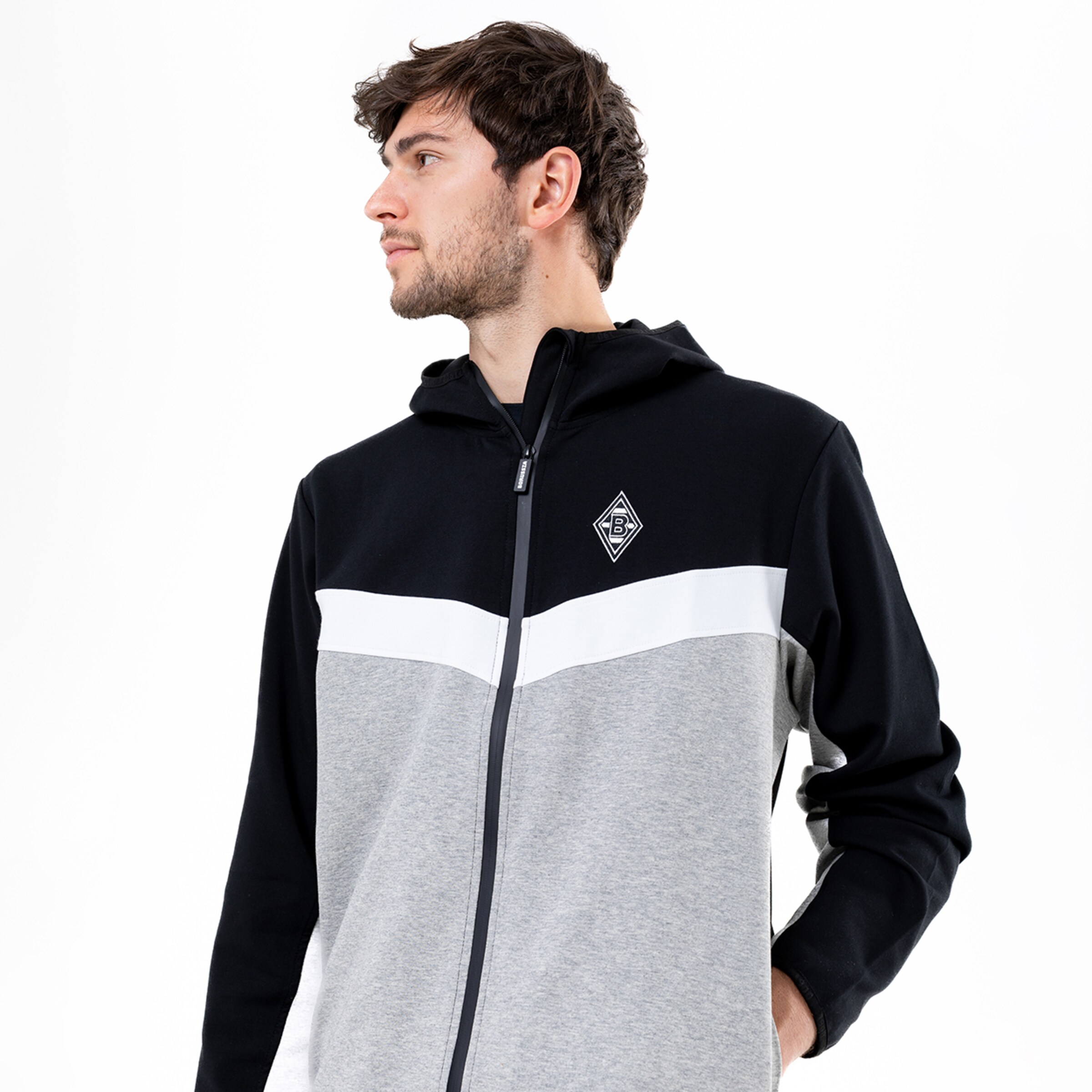 Ein Mann in einem grauen und schwarzen Trainingsanzug mit Kapuze betrachtet nach rechts.