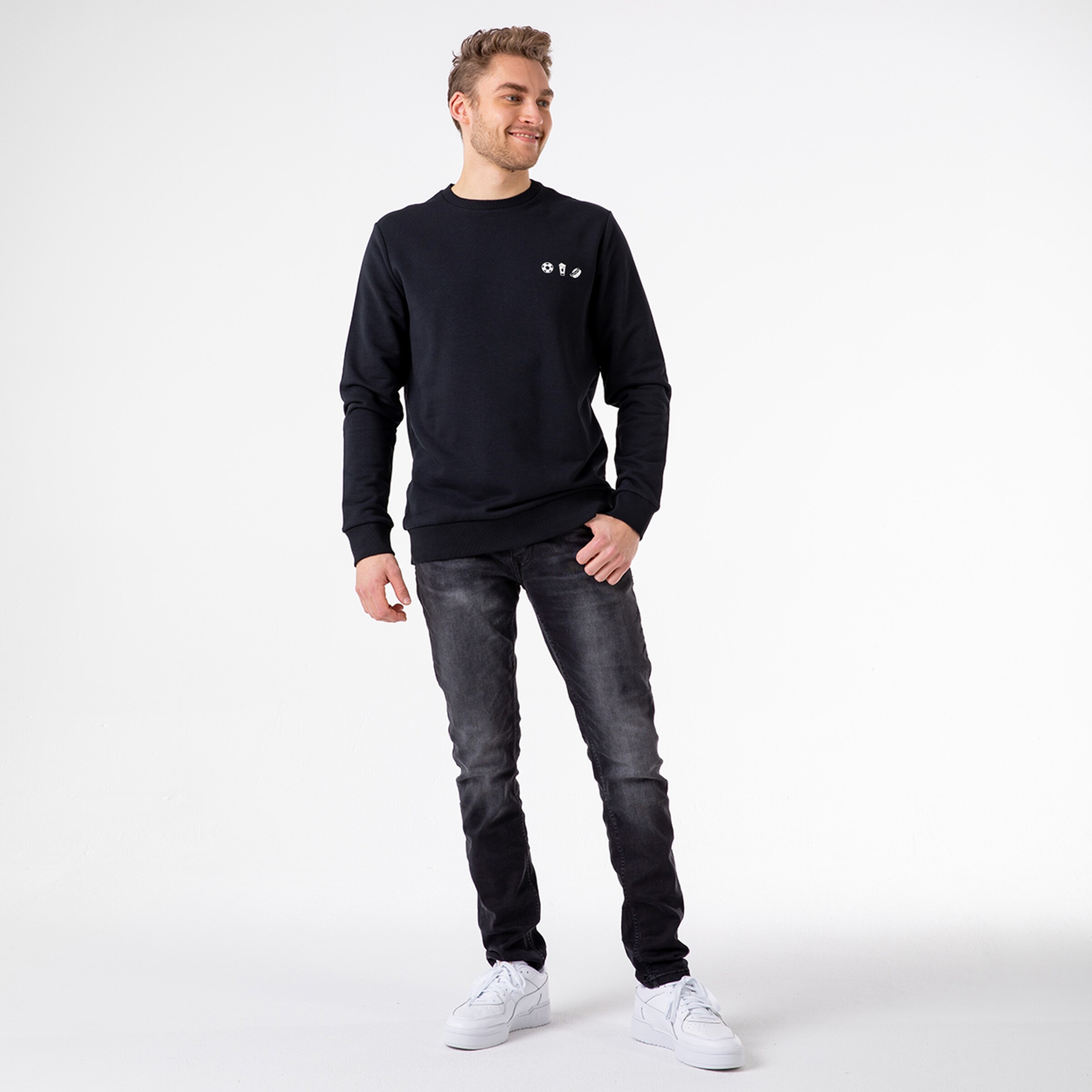Junger Mann steht in lässigem Outfit mit schwarzem Pullover und Jeans.