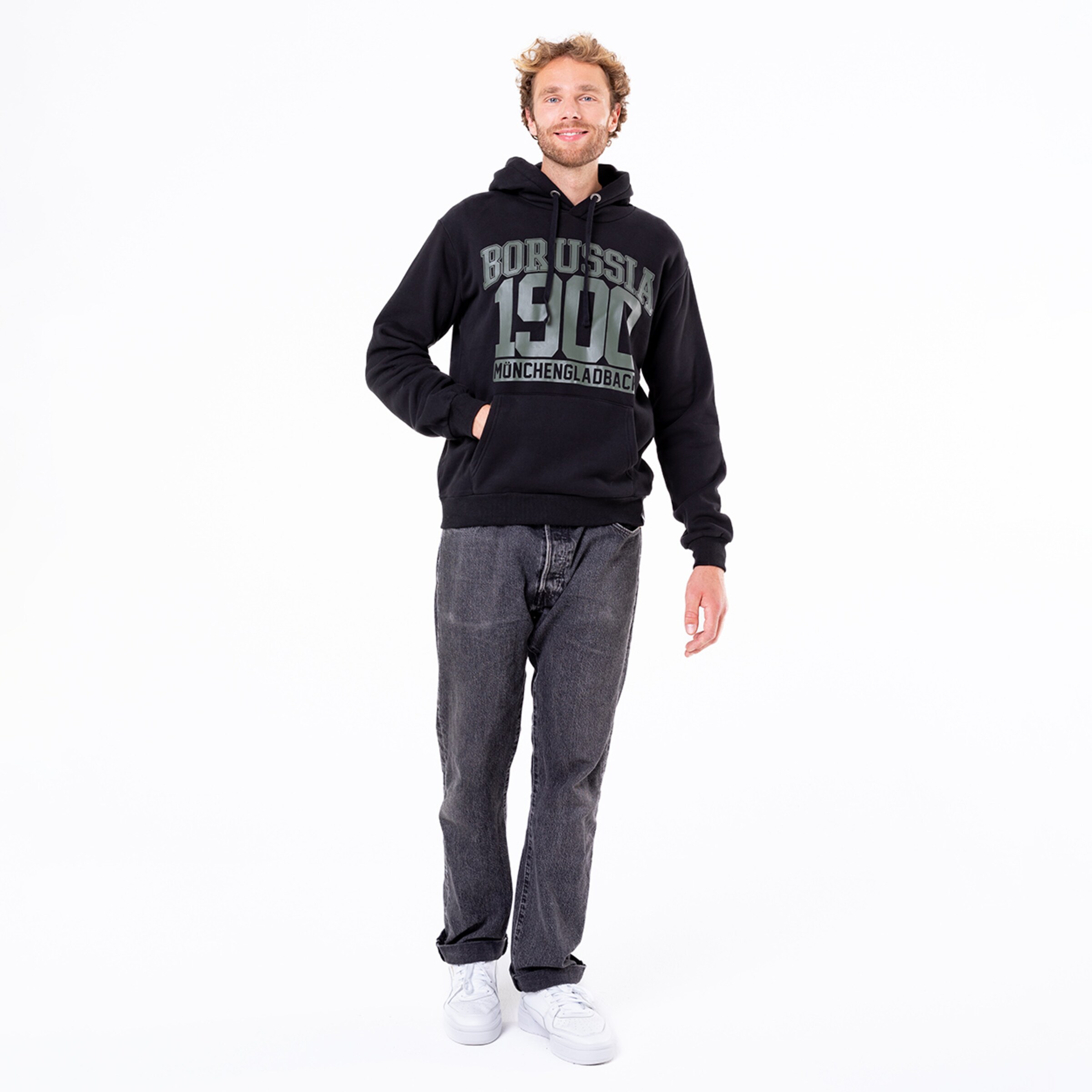 Mann in schwarzem Hoodie mit Aufdruck Borussia Mönchengladbach 1900 und grauen Jeans.
