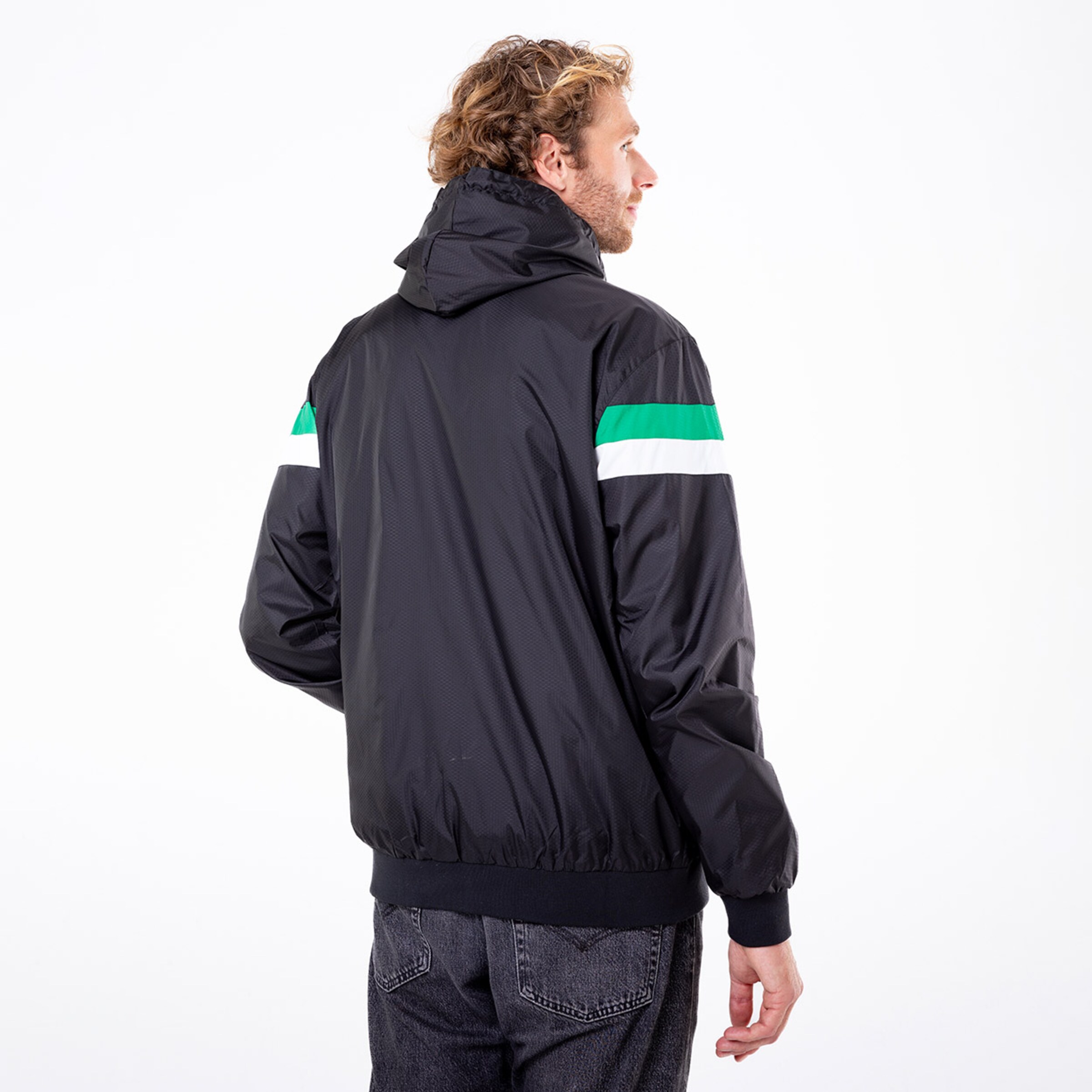 Mann steht mit dem Rücken zu sehen in schwarzer Jacke mit grünen und weißen Streifen.