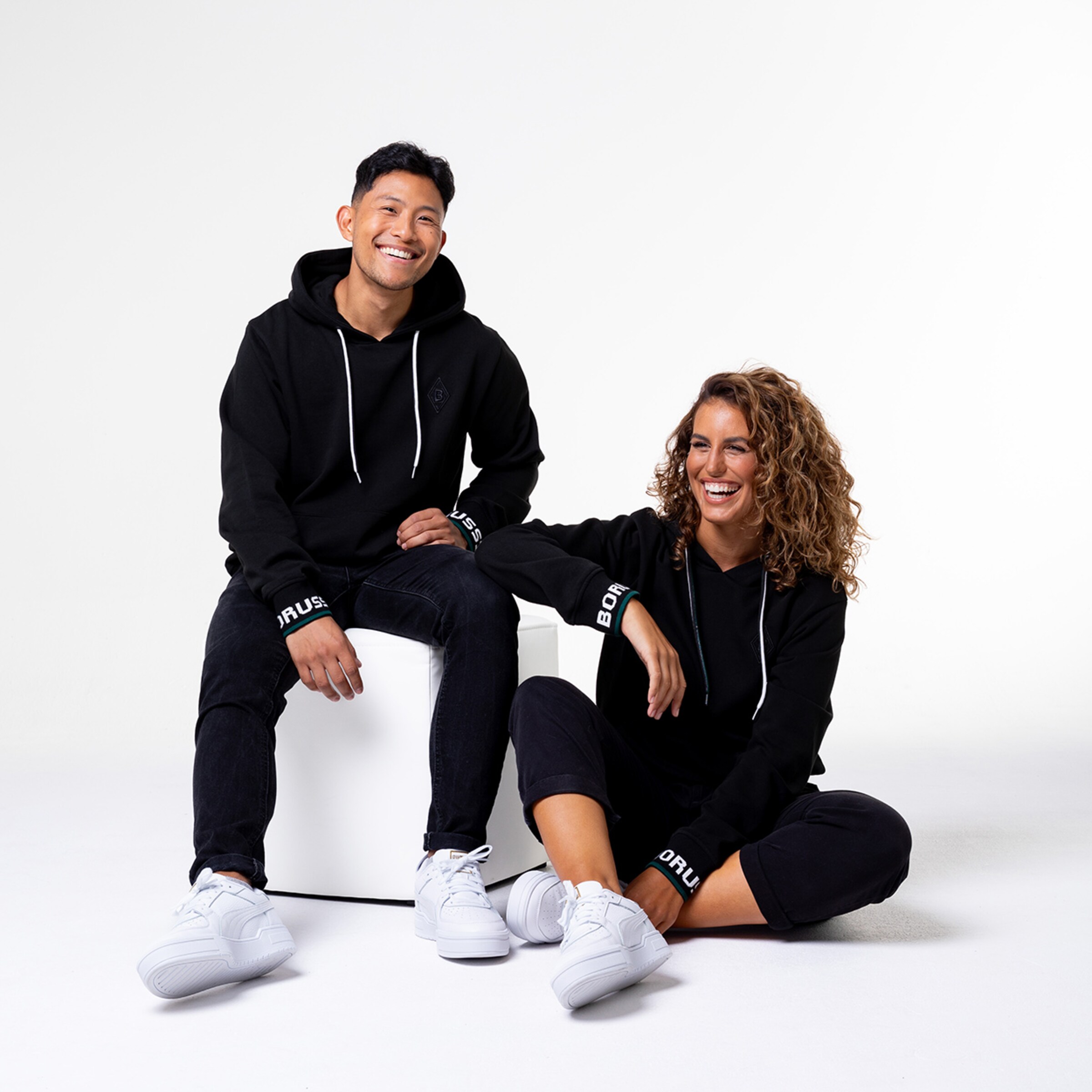 Two models wearing black hoodies with Borussia text and white sneakers.