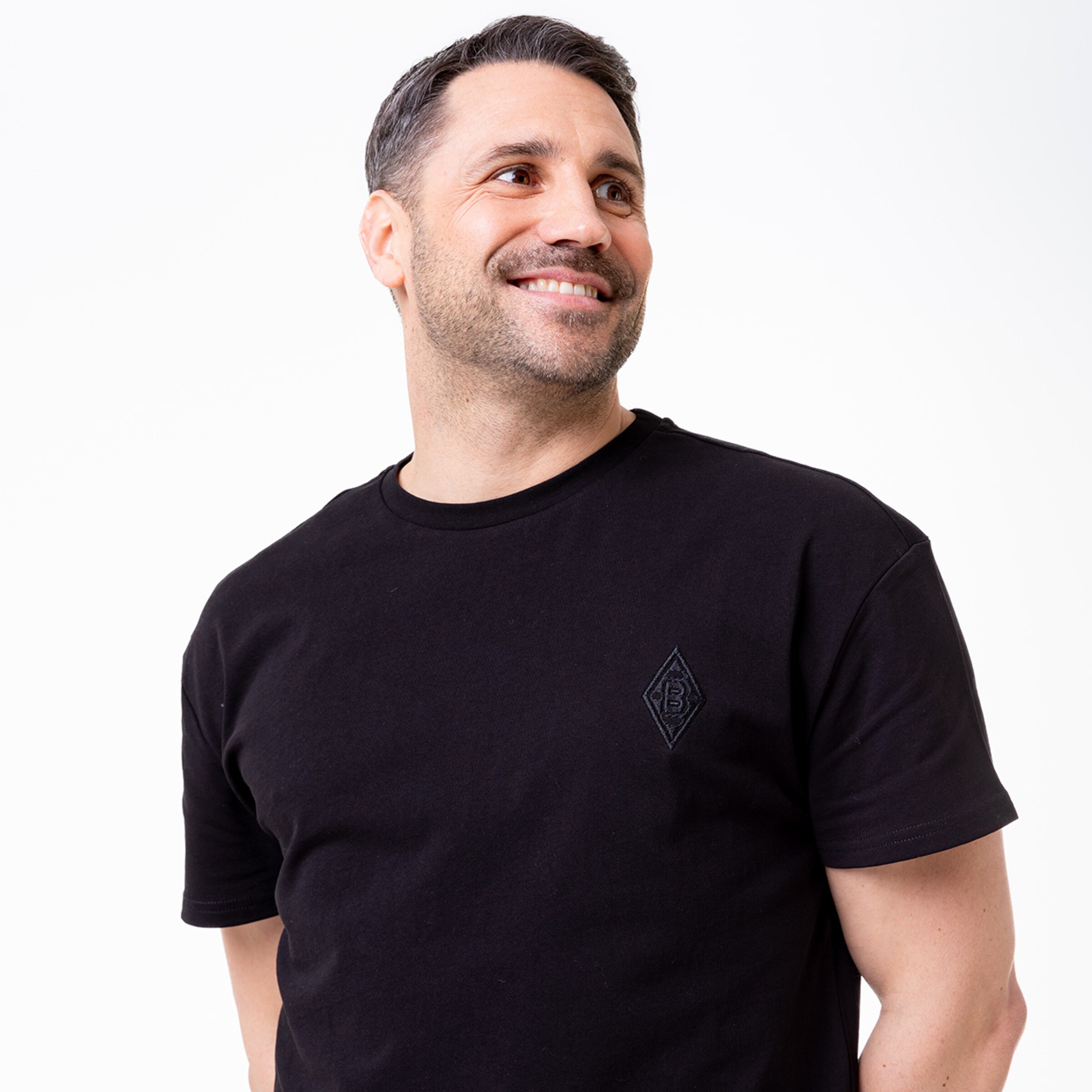 Mann mit kurzem Haar und breitem Lächeln trägt ein schwarzes T-Shirt mit einem Logo.
