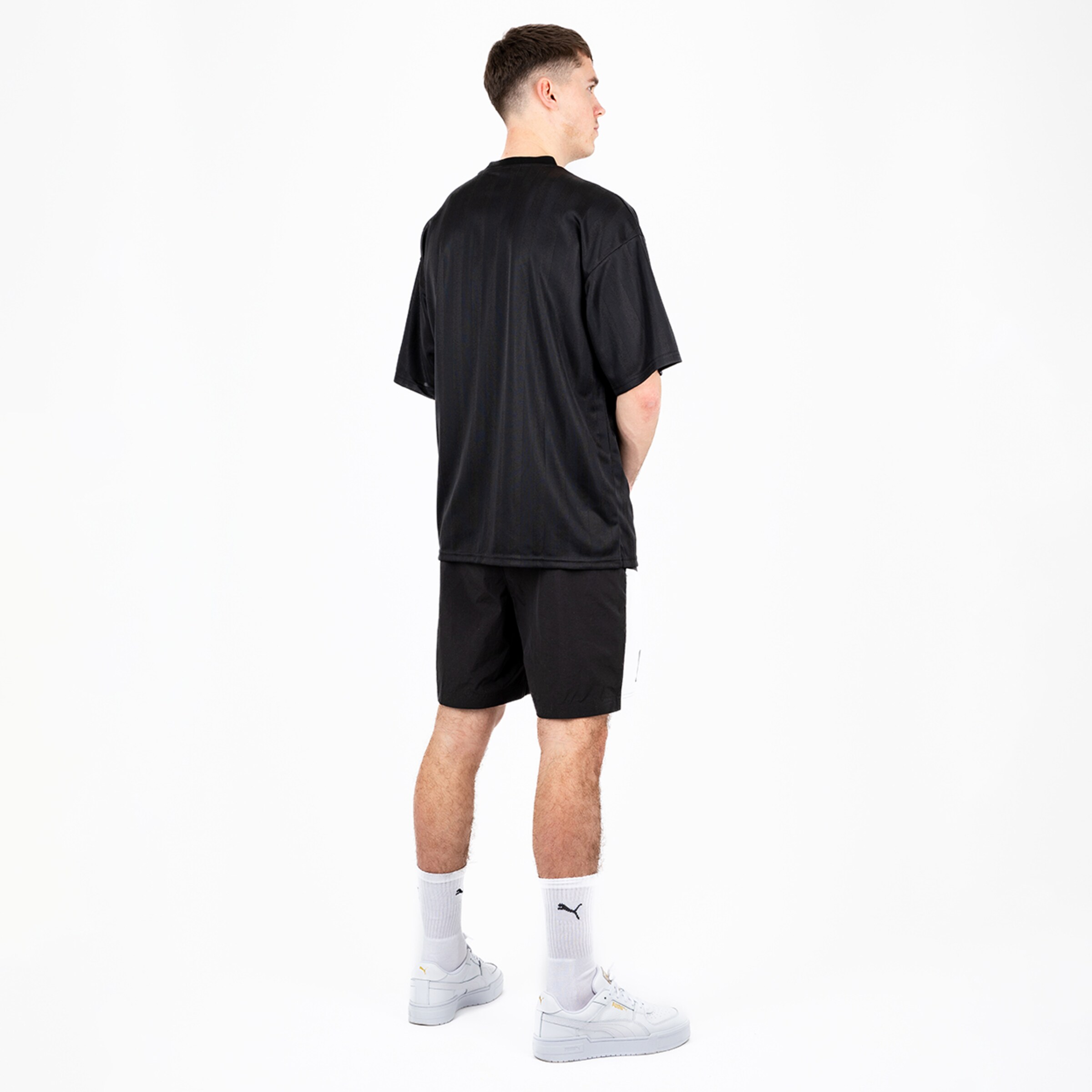 Mann von hinten in schwarzem T-Shirt und Shorts mit weißen Socken und Schuhen.
