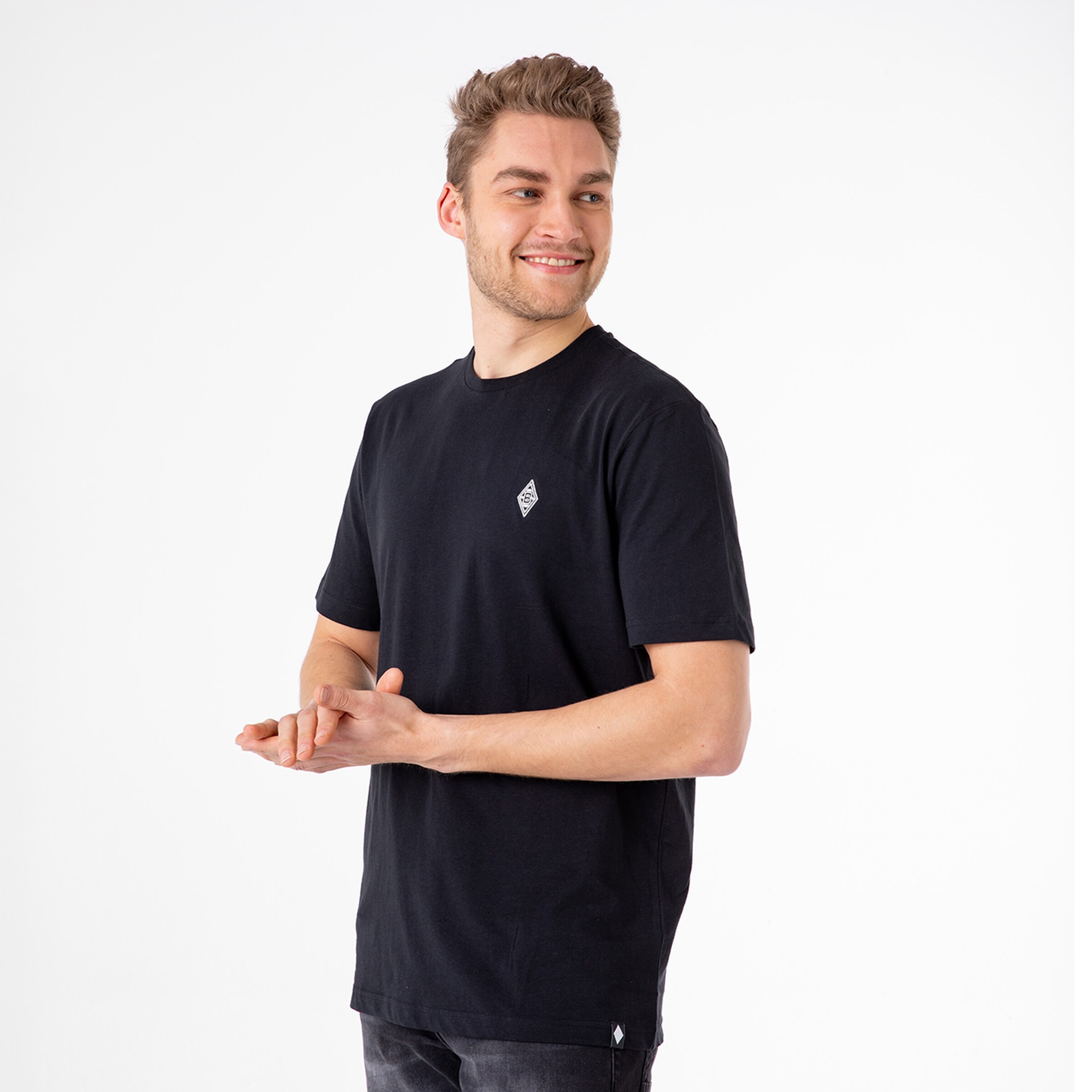 Man in black T-shirt with Borussia Mönchengladbach logo standing and smiling with slightly bent hands.