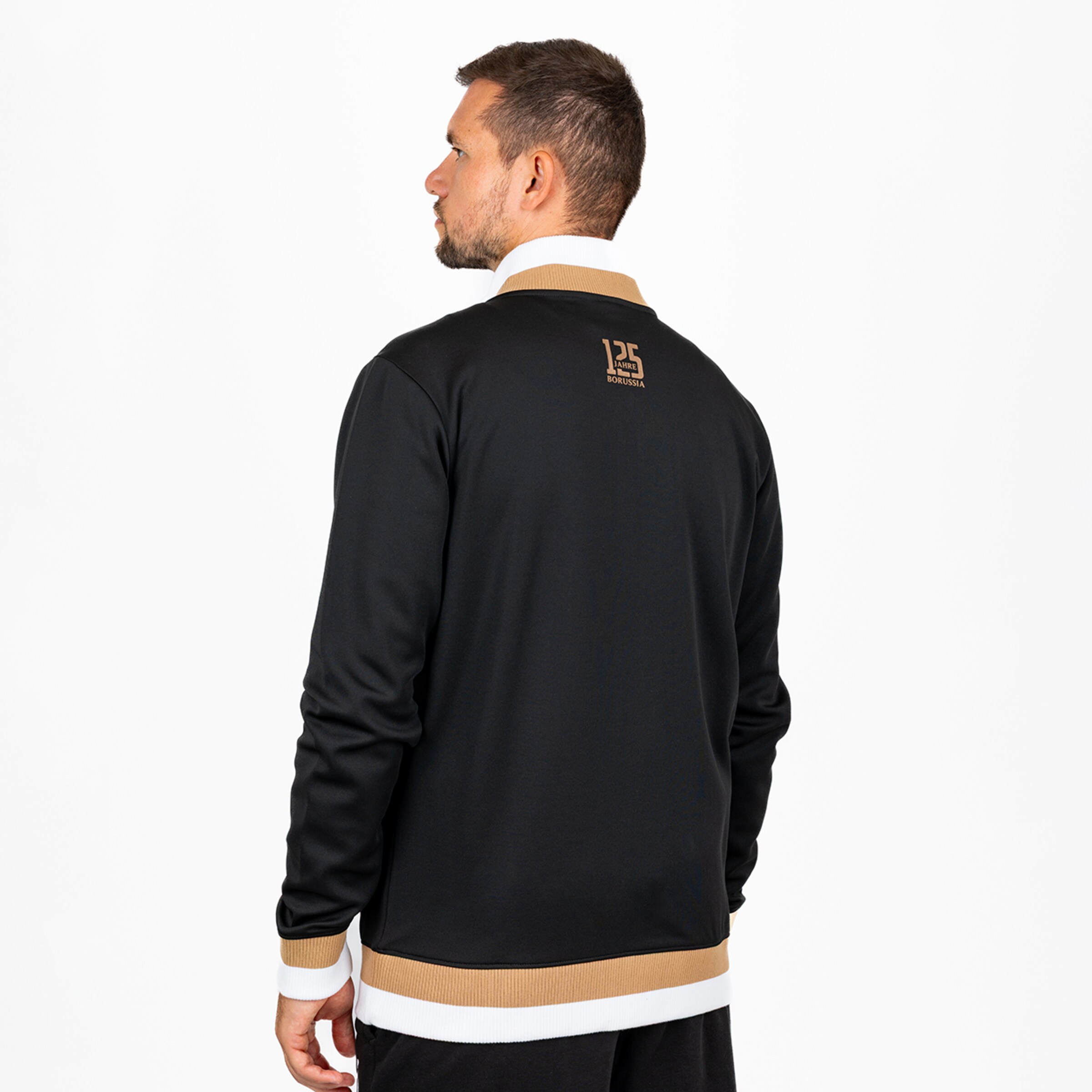 Rückansicht eines Mannes in schwarzer Trainingsjacke mit gold-weißen Bündchen und „125 JAHRE BORUSSIA“-Logo auf dem Rücken.