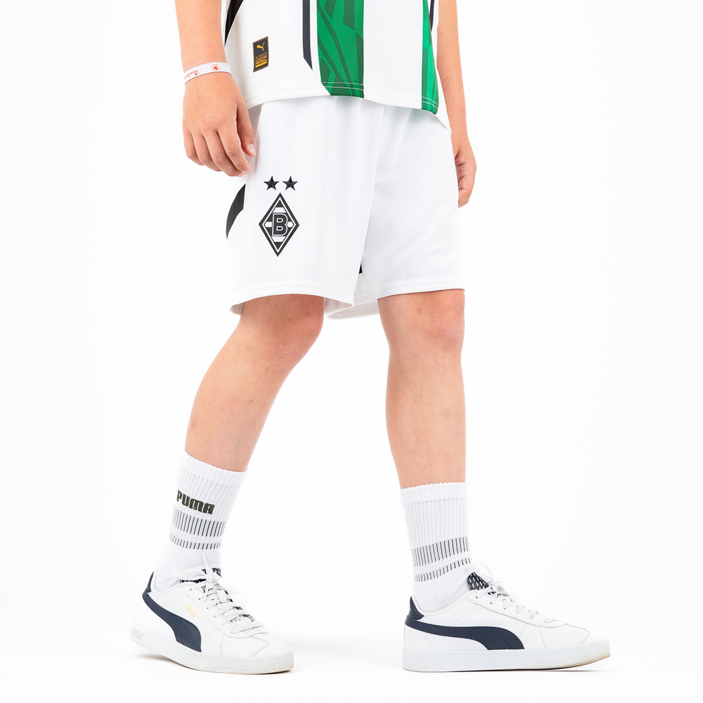 A child wearing white soccer shorts with Borussia Mönchengladbach logo and two stars paired with white socks and sneakers.