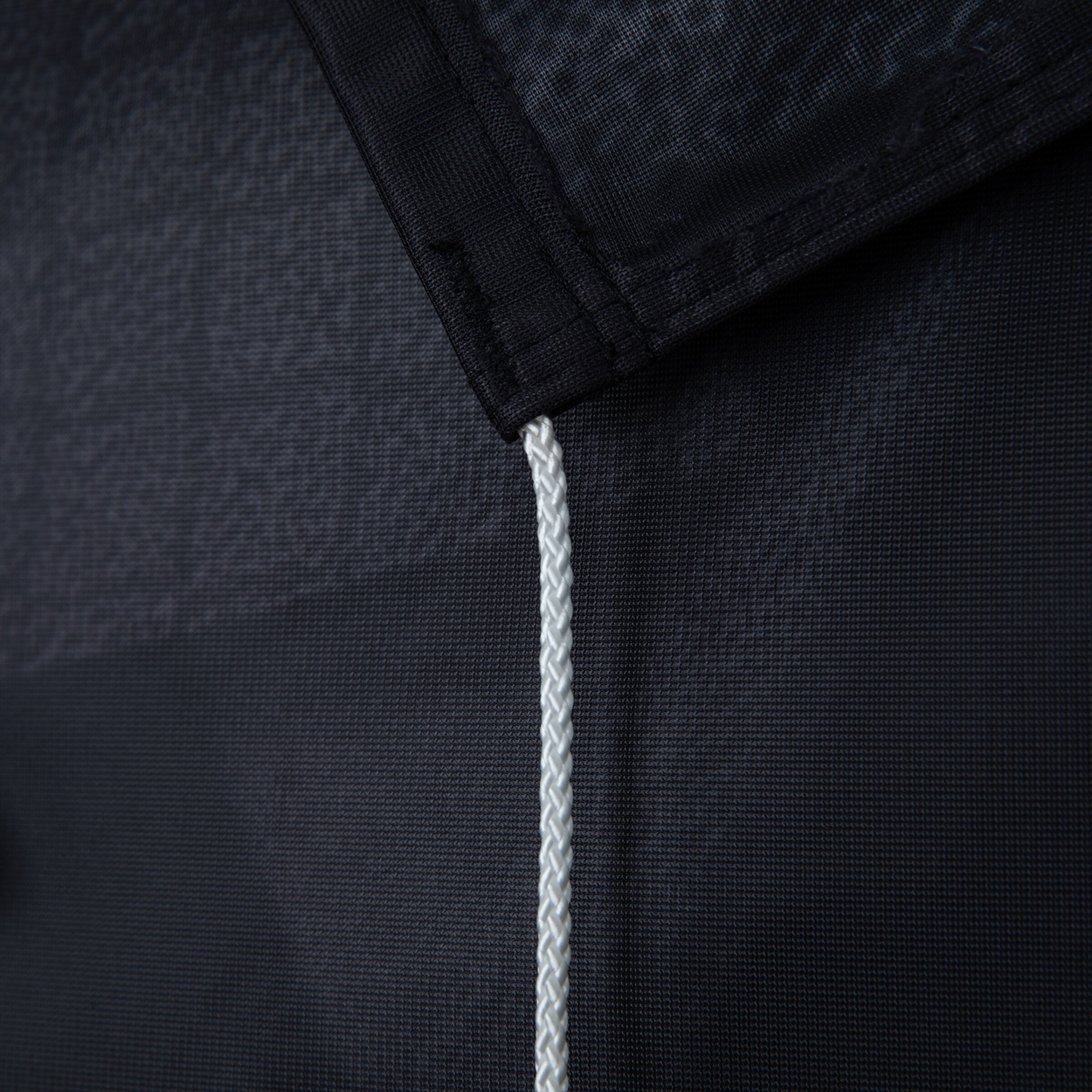 Detailaufnahme einer schwarzen Textilplane mit verstärktem Saum und einer weißen, geflochtenen Kordel an der Ecke.