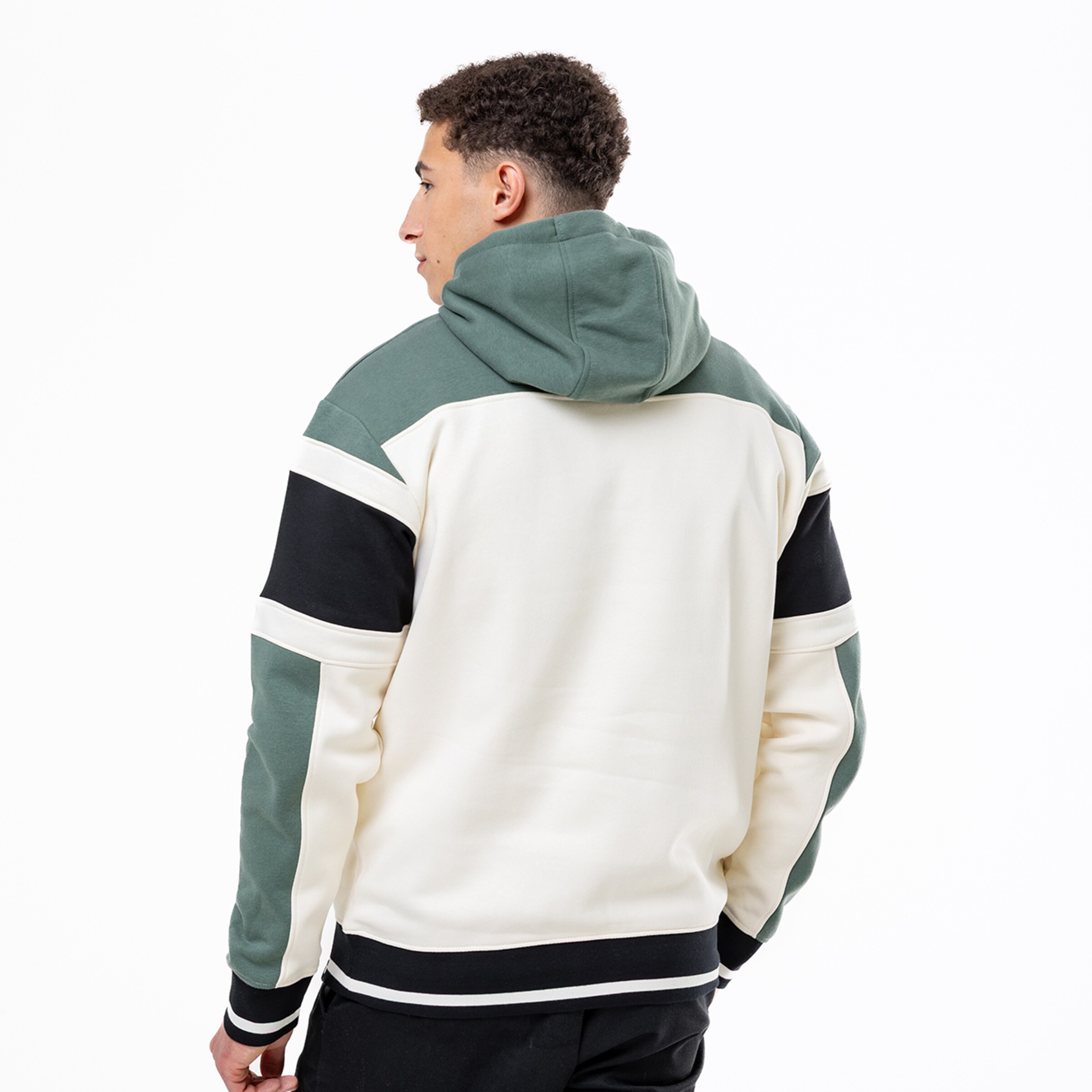 Rückansicht eines Mannes in einem Hoodie mit Blockfarben in Creme, Salbeigrün und Schwarz vor weißem Hintergrund.