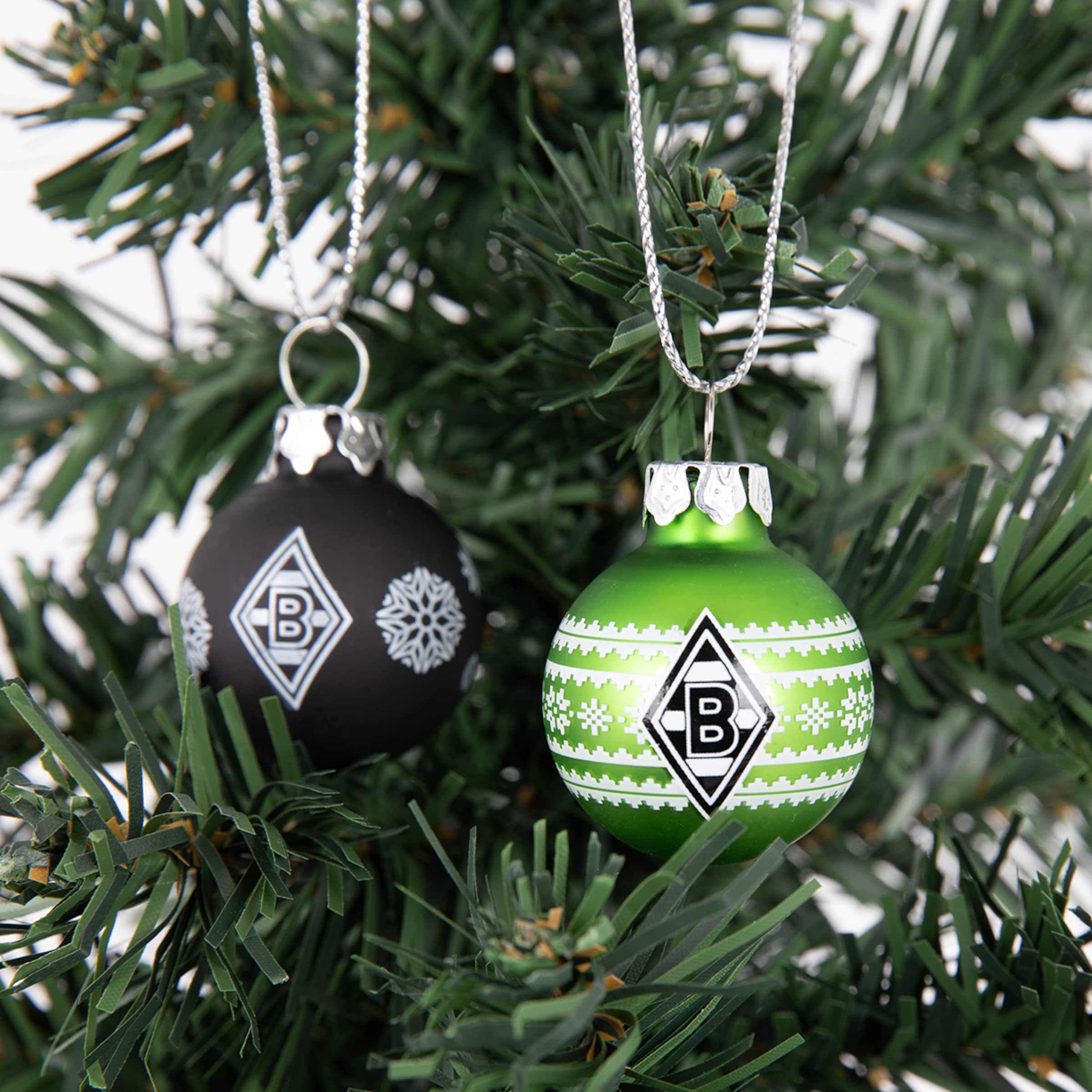 Schwarze und grüne Weihnachtskugeln mit dem Borussia Mönchengladbach Logo hängen an einem künstlichen Tannenbaum.