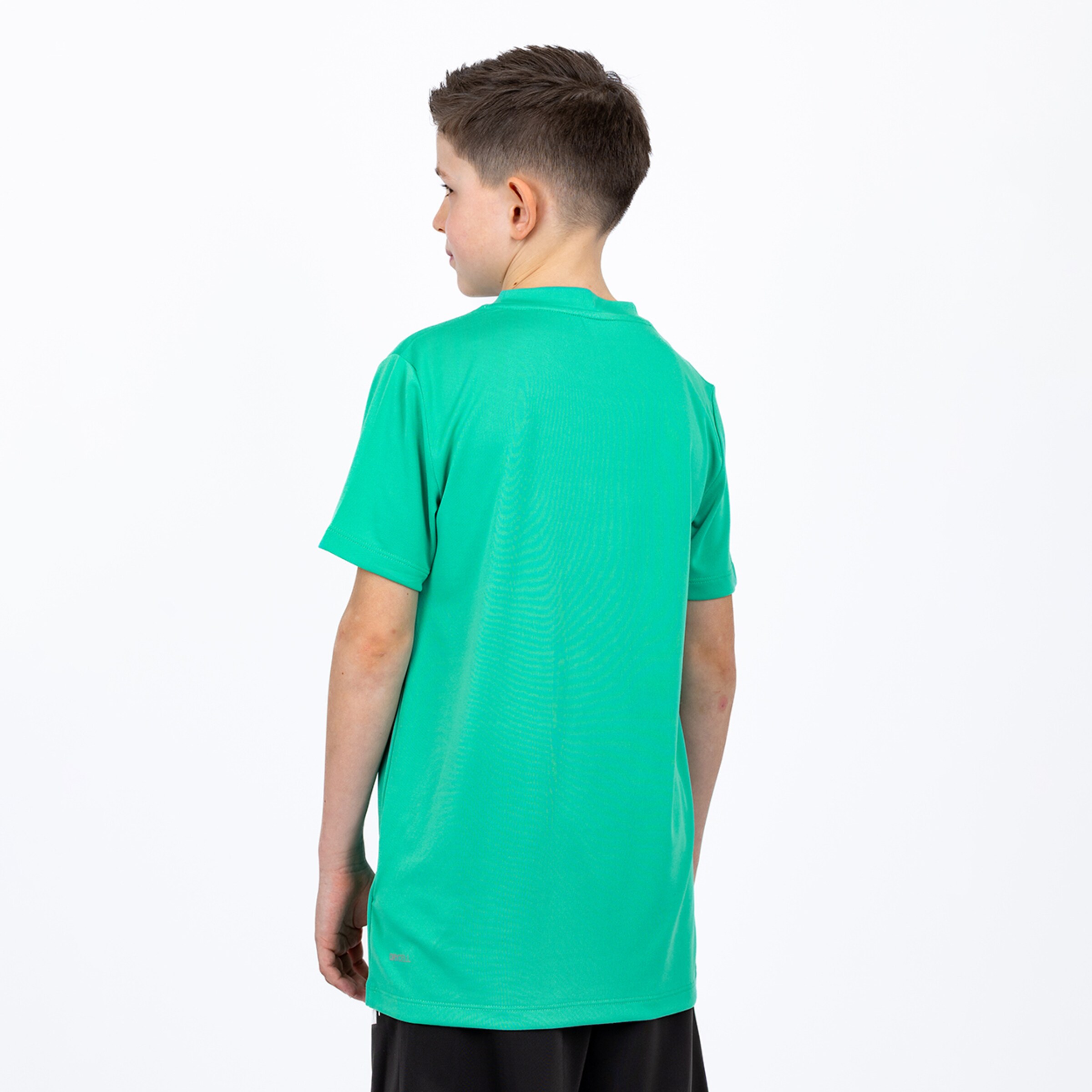 Back view of a boy wearing a green short-sleeved t-shirt and black shorts against a white background.