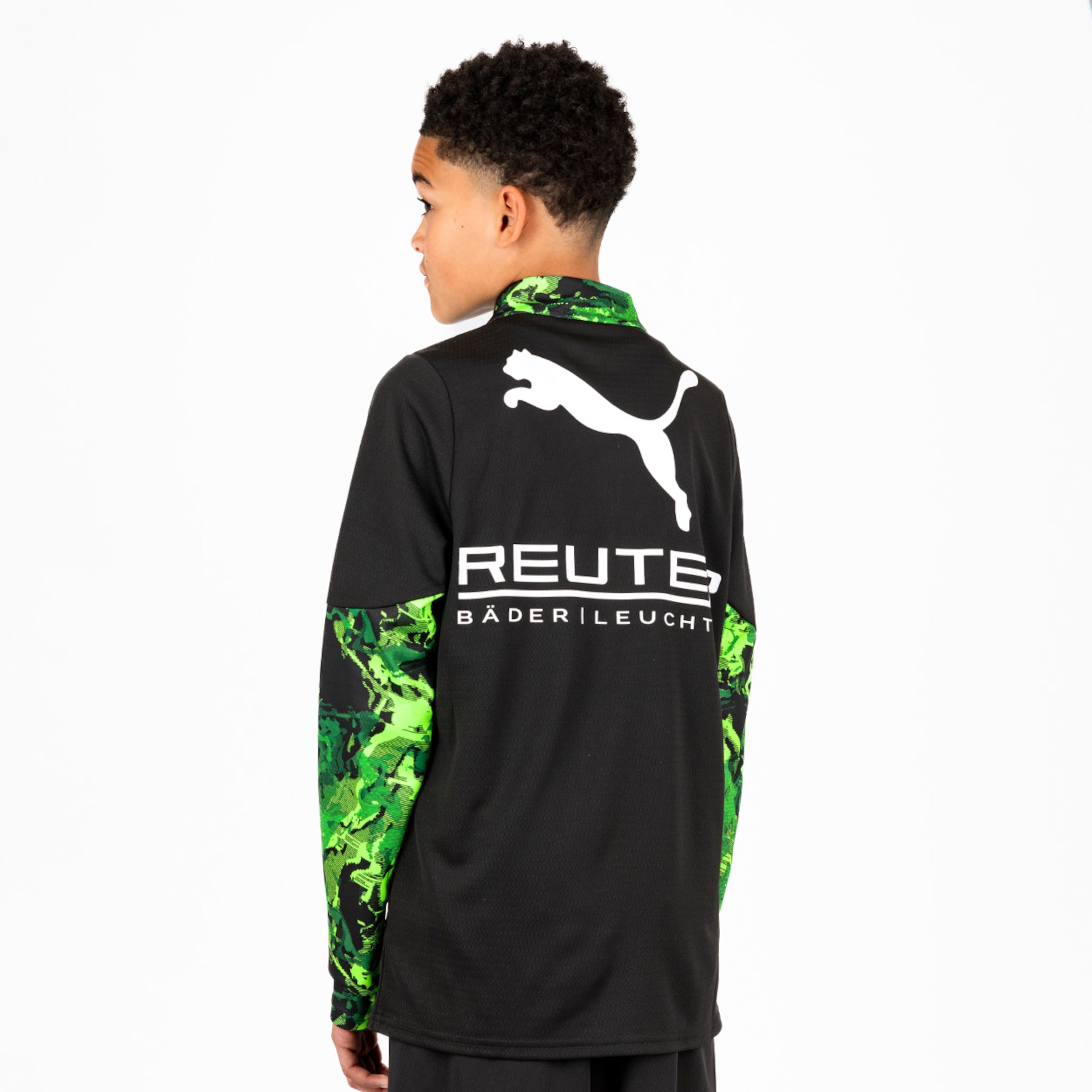 Rückansicht eines Jungen in einem schwarzen Puma-Shirt mit grün gemusterten Ärmeln und weißem „REUTE BÄDER