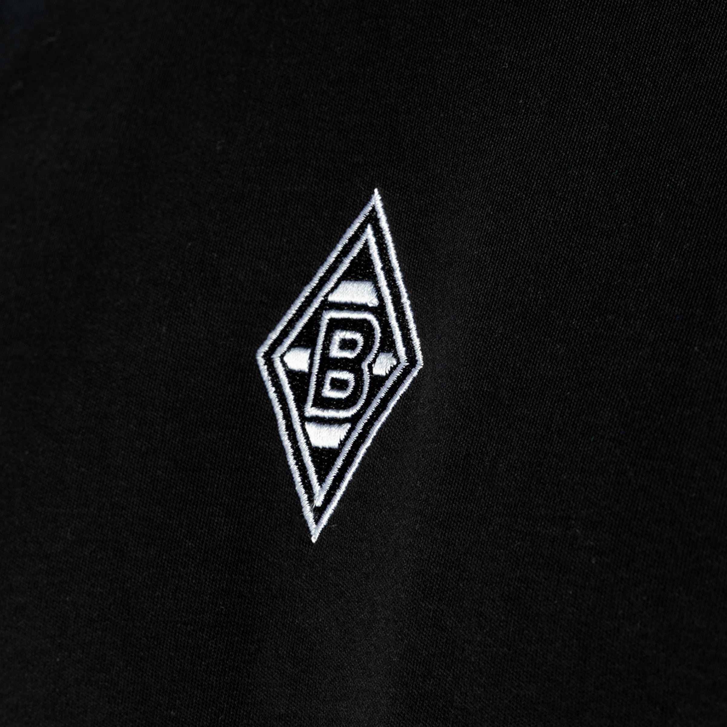 Weiß gesticktes Logo von Borussia Mönchengladbach (Raute mit einem B) auf schwarzem Stoff.