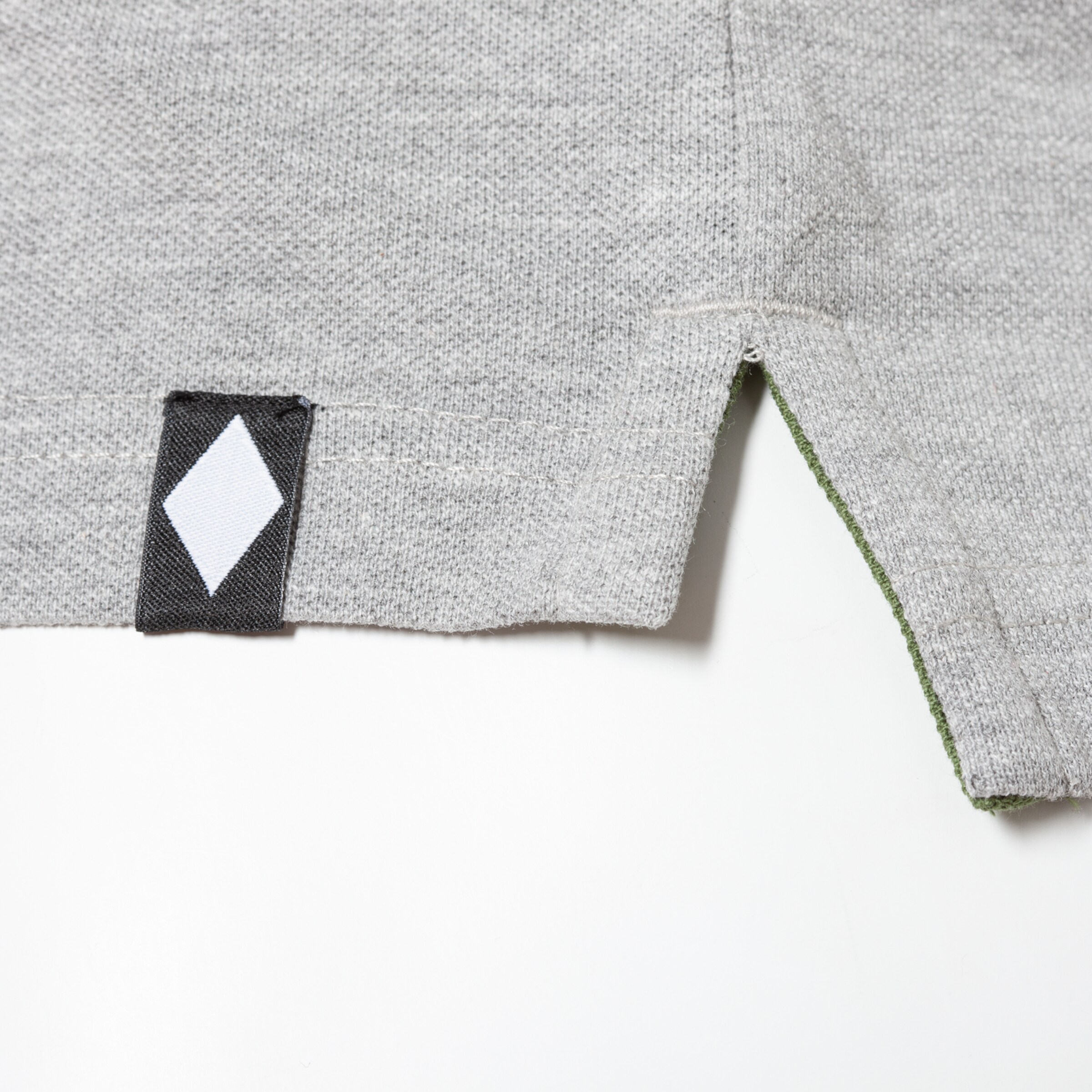Detailansicht des grauen T-Shirts mit schwarzem Aufnäher und weißem rhombischen Design.