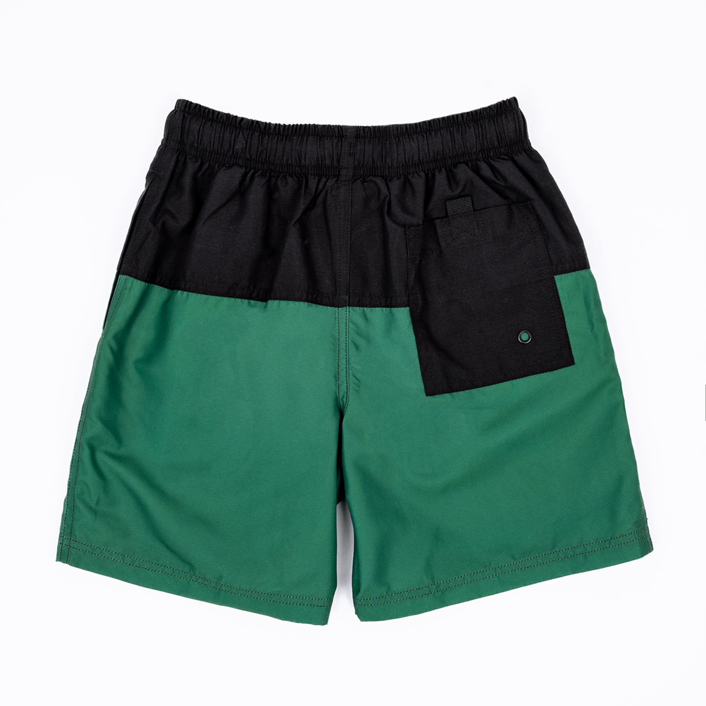 Two-tone swim shorts, black on the upper half and a deep emerald green on the lower half, featuring an elastic black waistband and a black back pocket with a drainage grommet, laid flat on a white background.