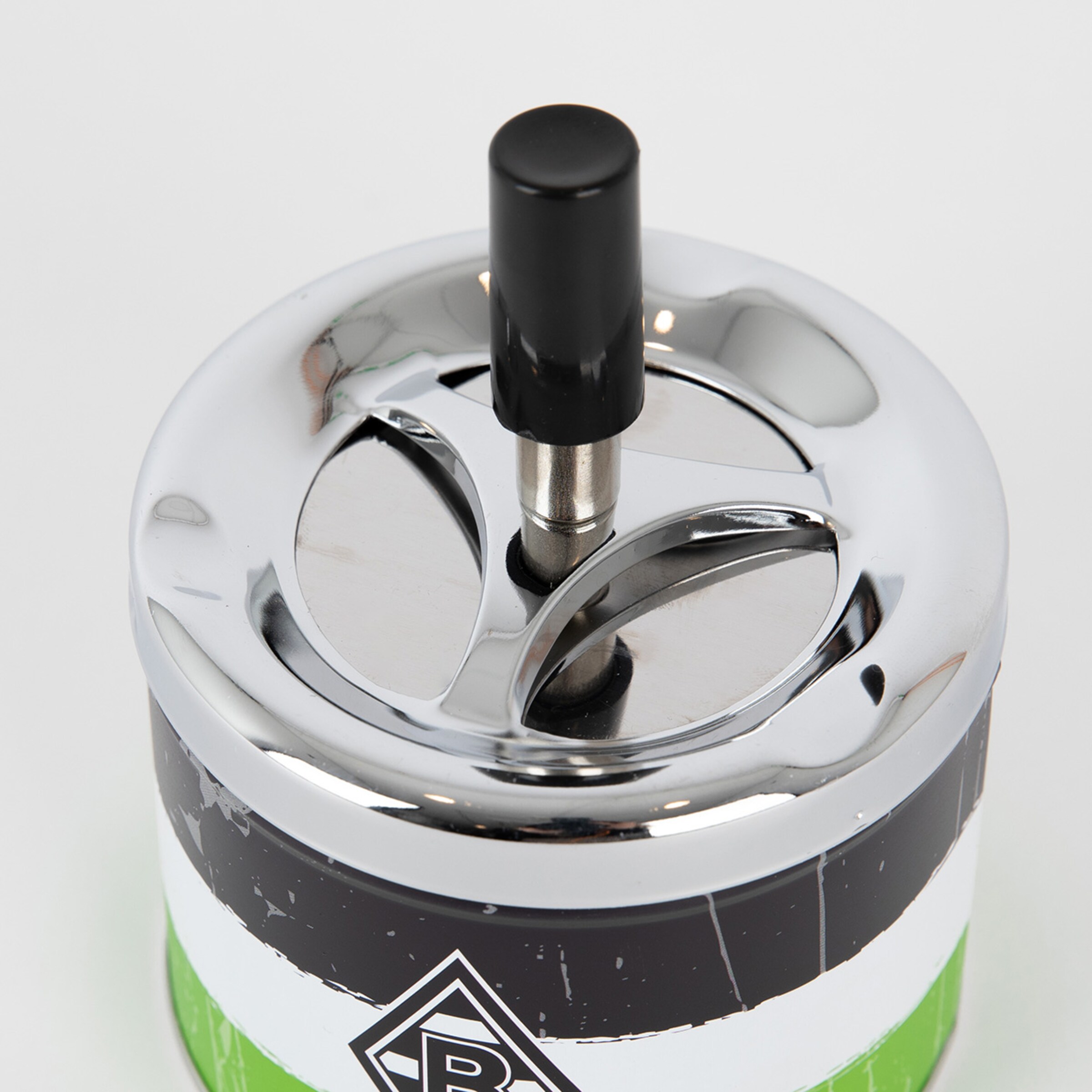 Nahaufnahme eines silbernen Drehaschenbechers mit schwarzem Druckknopf und grün-weiß-schwarzem Gehäuse auf weißem Hintergrund.