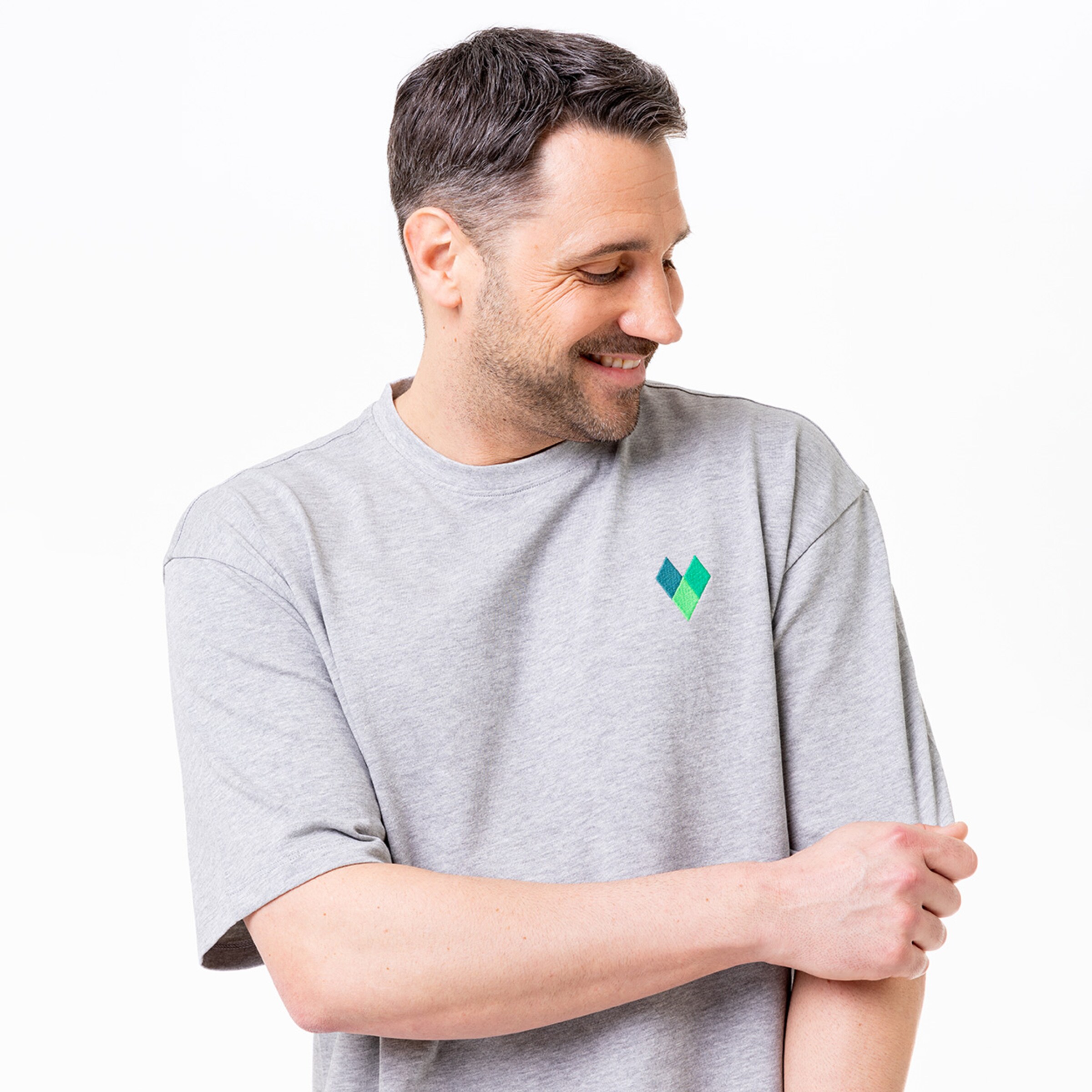 Mann trägt graues T-Shirt mit grünem geometrischem Logo auf der Brust.