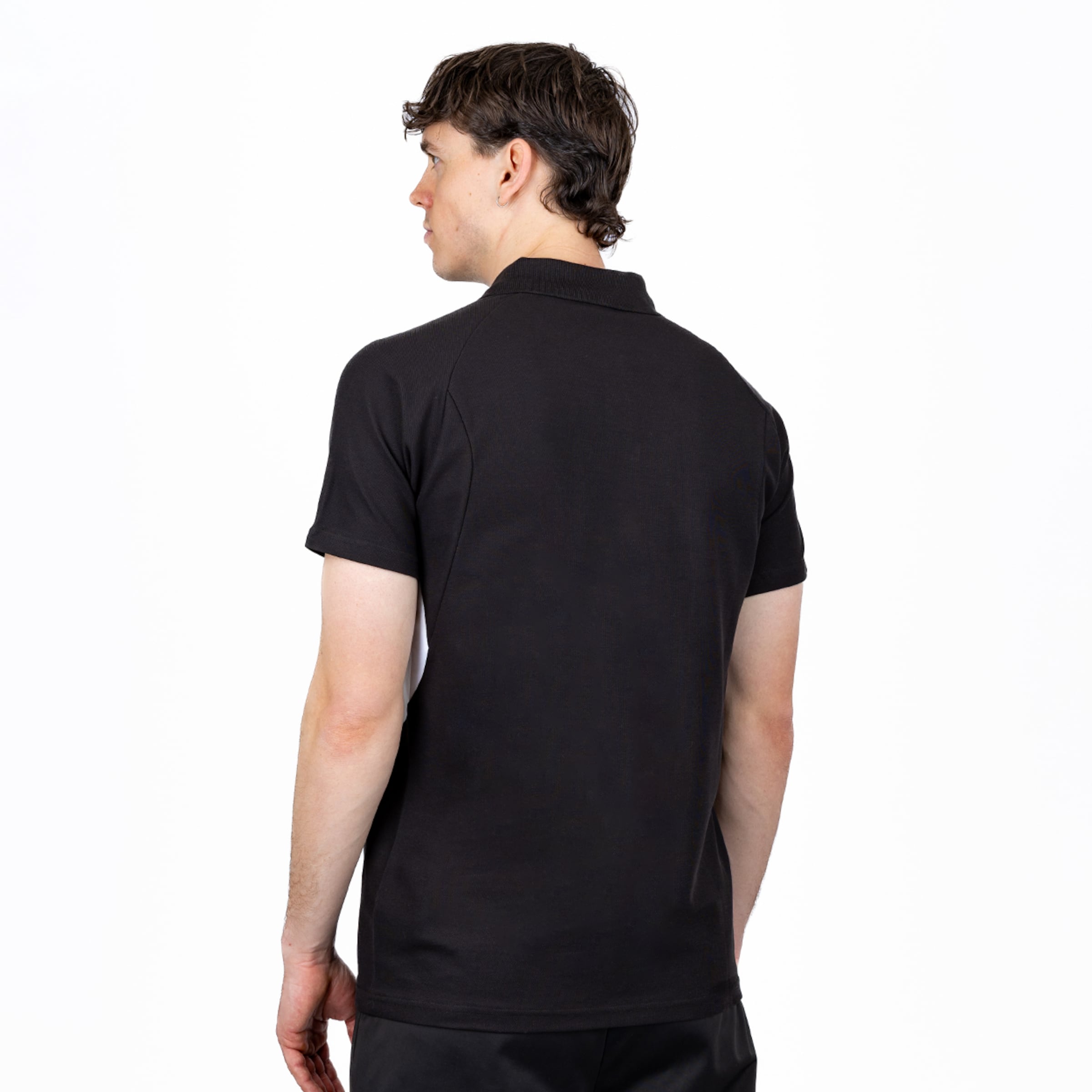 Rücken- und Seitenansicht eines männlichen Models, das ein schwarzes, kurzärmeliges Poloshirt und eine schwarze Hose vor einem weißen Hintergrund trägt und nach links blickt.