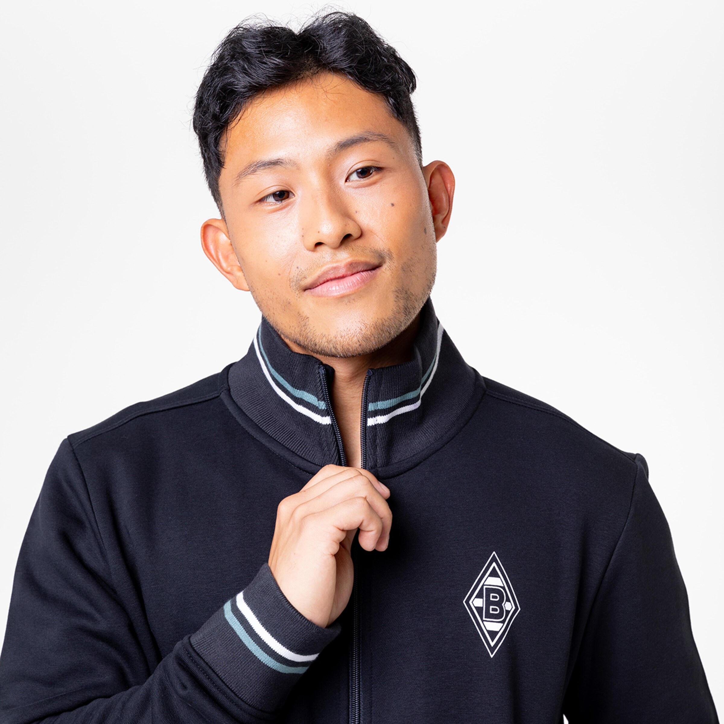 Mann mit kurzem schwarzem Haar in einem schwarzen Trainingsjacke mit Logo.