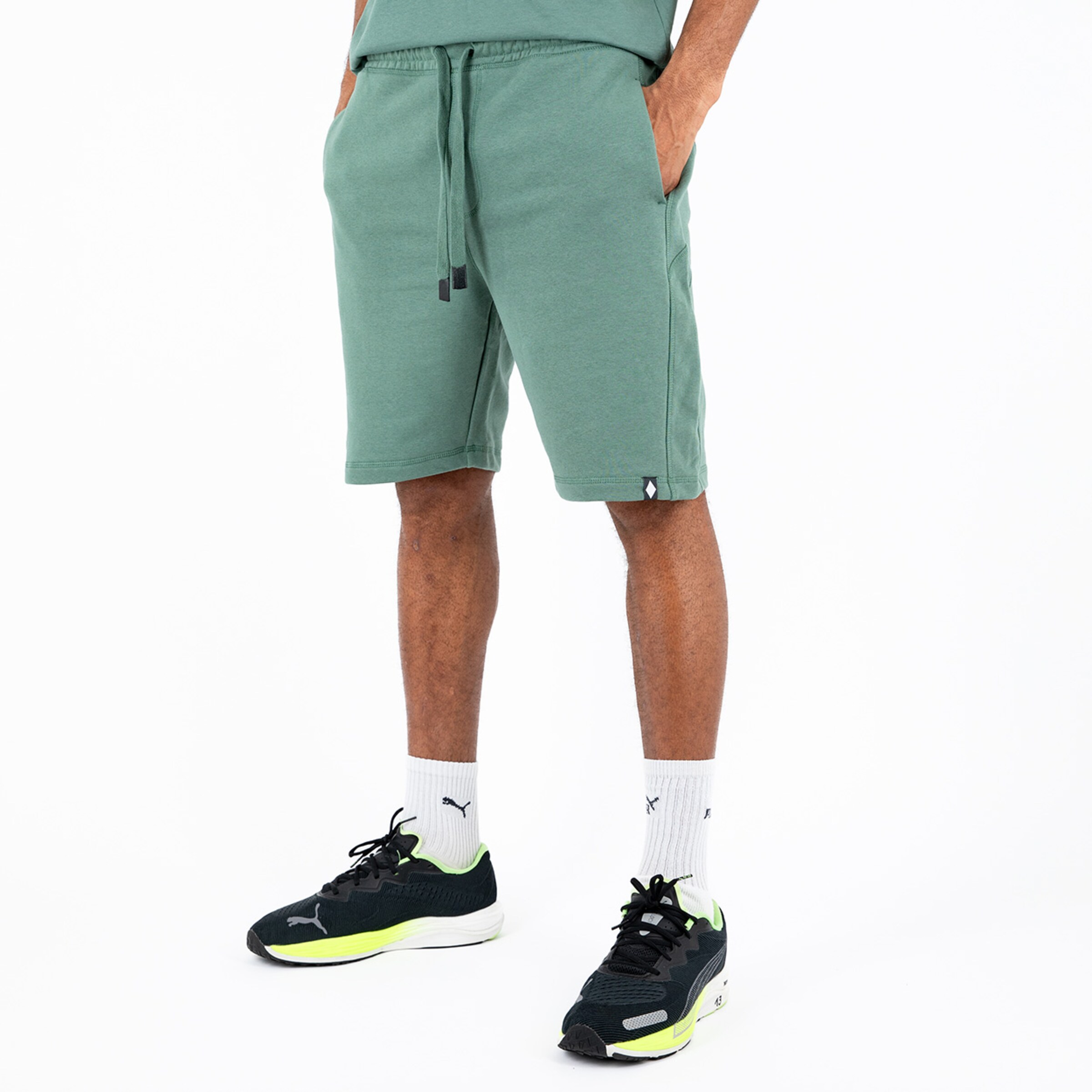 Mann trägt grüne Sportshorts und schwarze Sneakers.