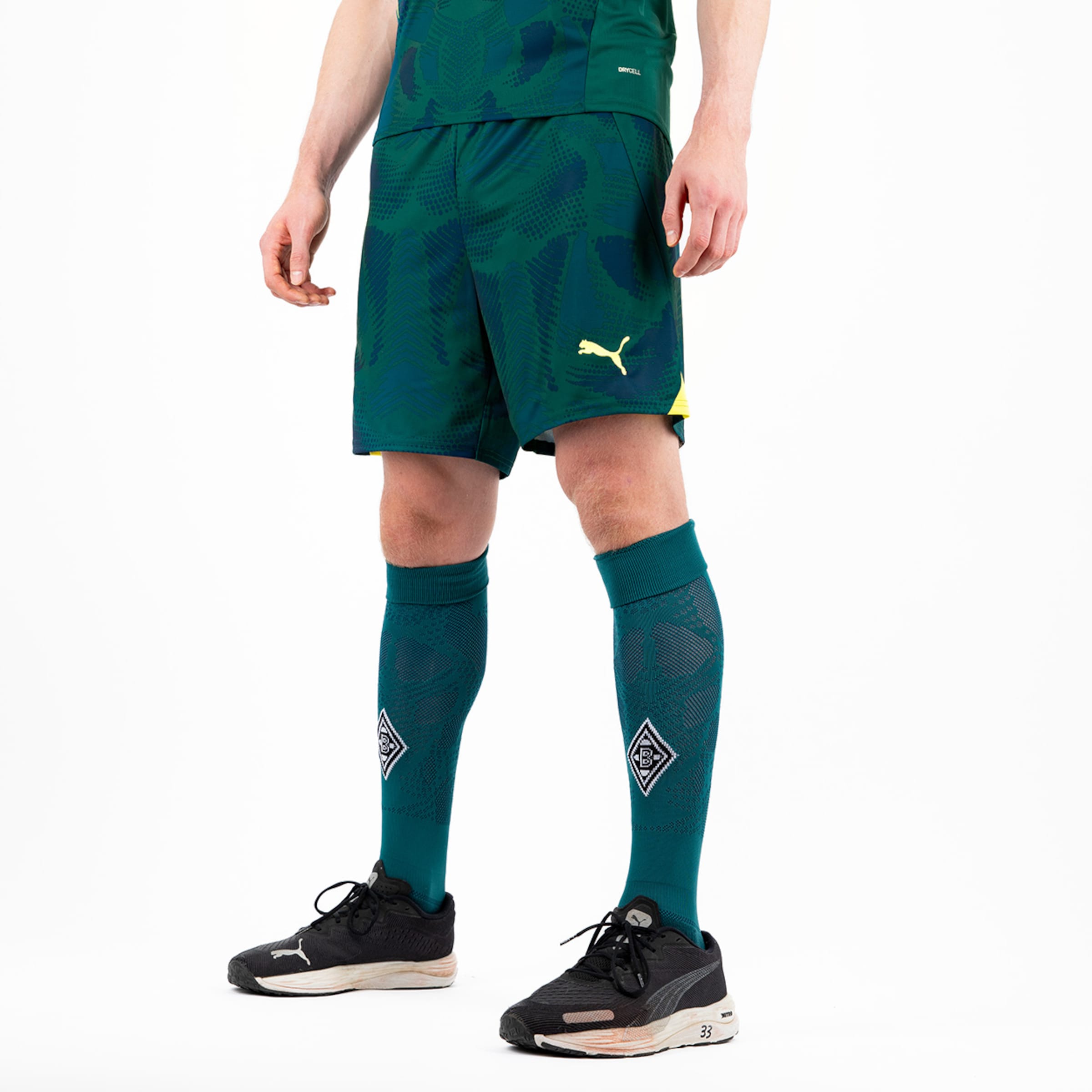 Mann trägt grüne Fußballshorts und Socken von Puma.
