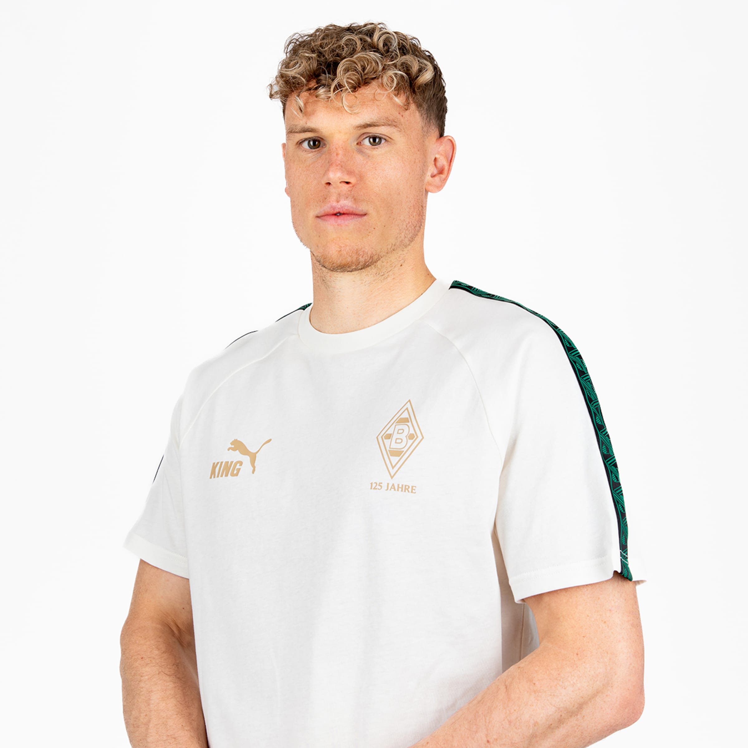 Porträt eines Mannes mit blonden Locken in einem weißen T-Shirt mit Borussia Mönchengladbach-Wappen und goldenem Puma-Logo.