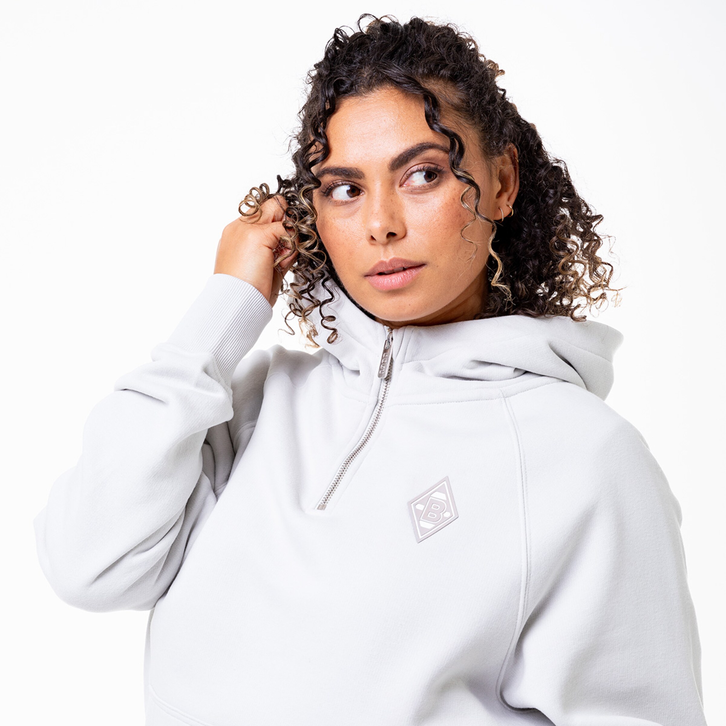 Frau mit lockigem Haar in grauem Hoodie mit Reißverschluss.