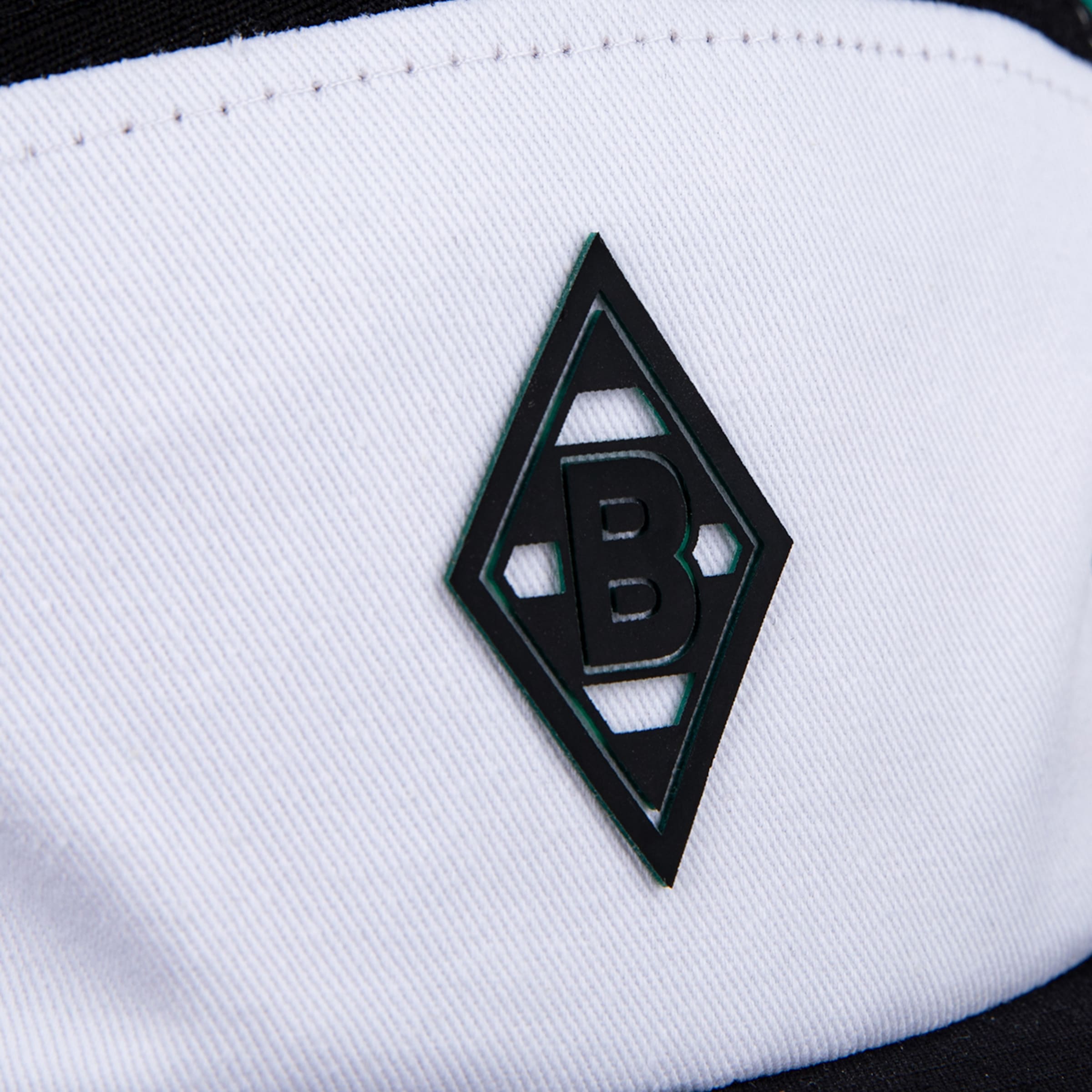 Detailansicht des Borussia Mönchengladbach Logos. Schwarzes Rauten-Wappen mit einem "B" auf weißem strukturiertem Stoff.