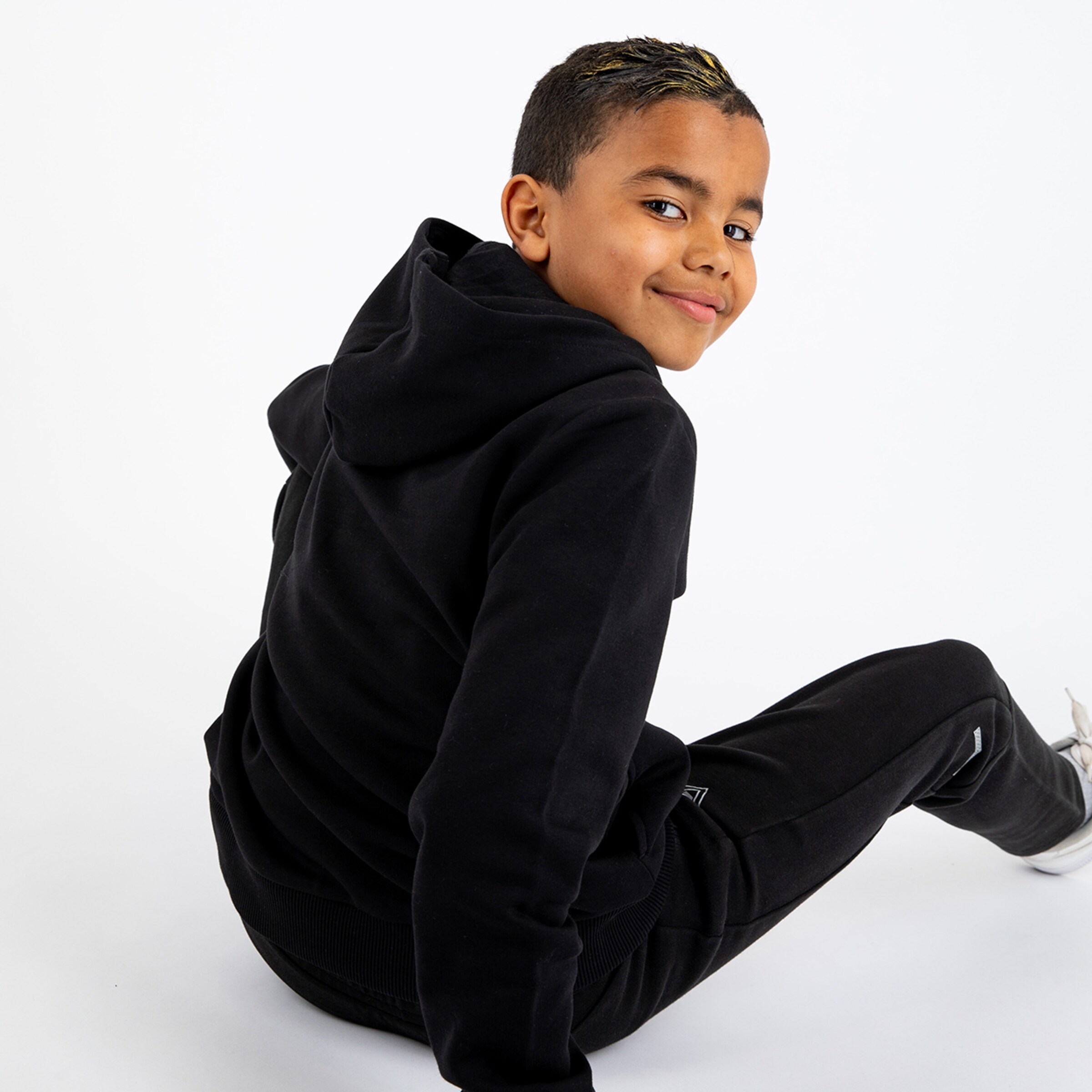 A boy with short dark hair and a friendly smile sits with his back to the camera wearing athletic clothing.
