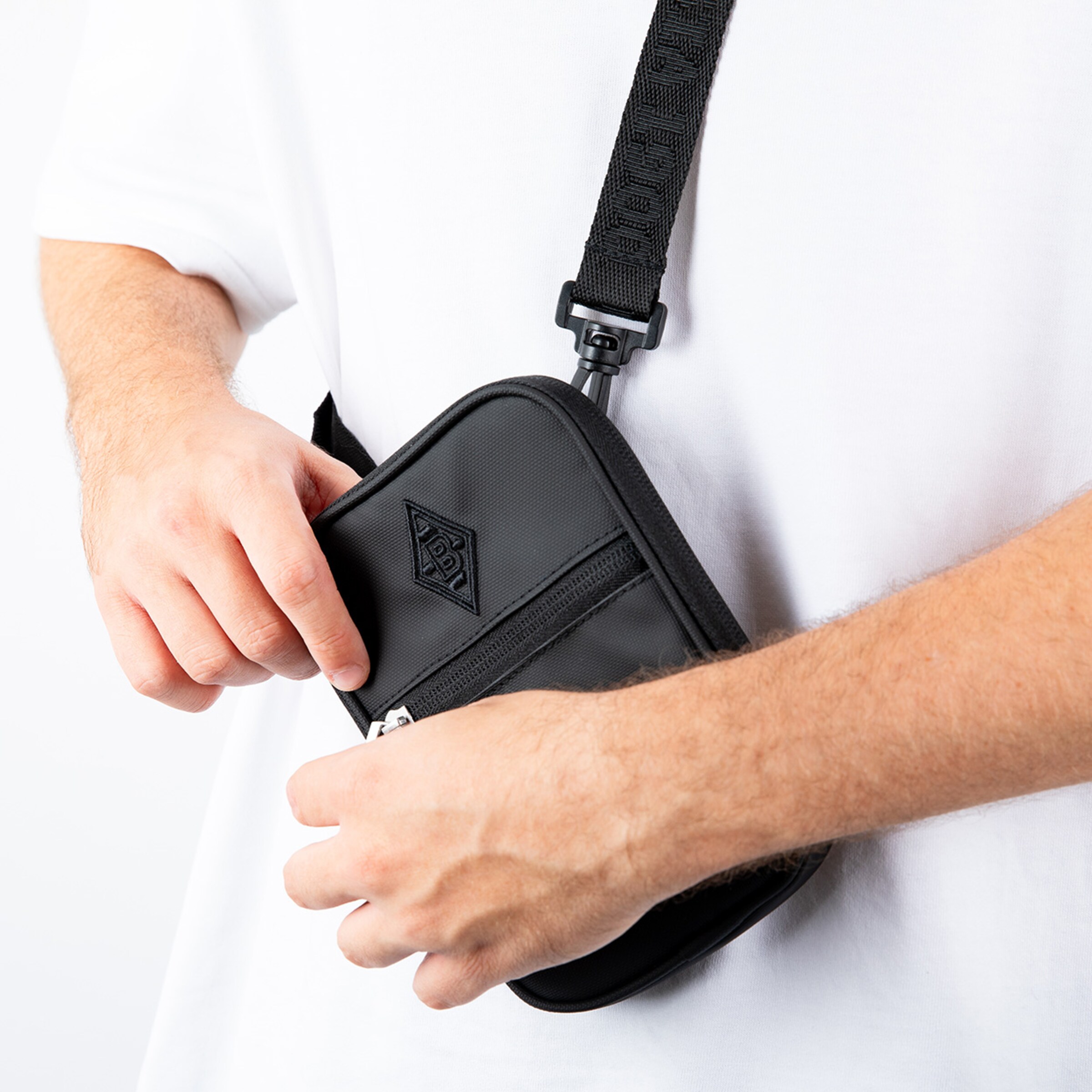 Schwarze Umhängetasche mit Reißverschluss getragen von einer Person in einem weißen T-Shirt.
