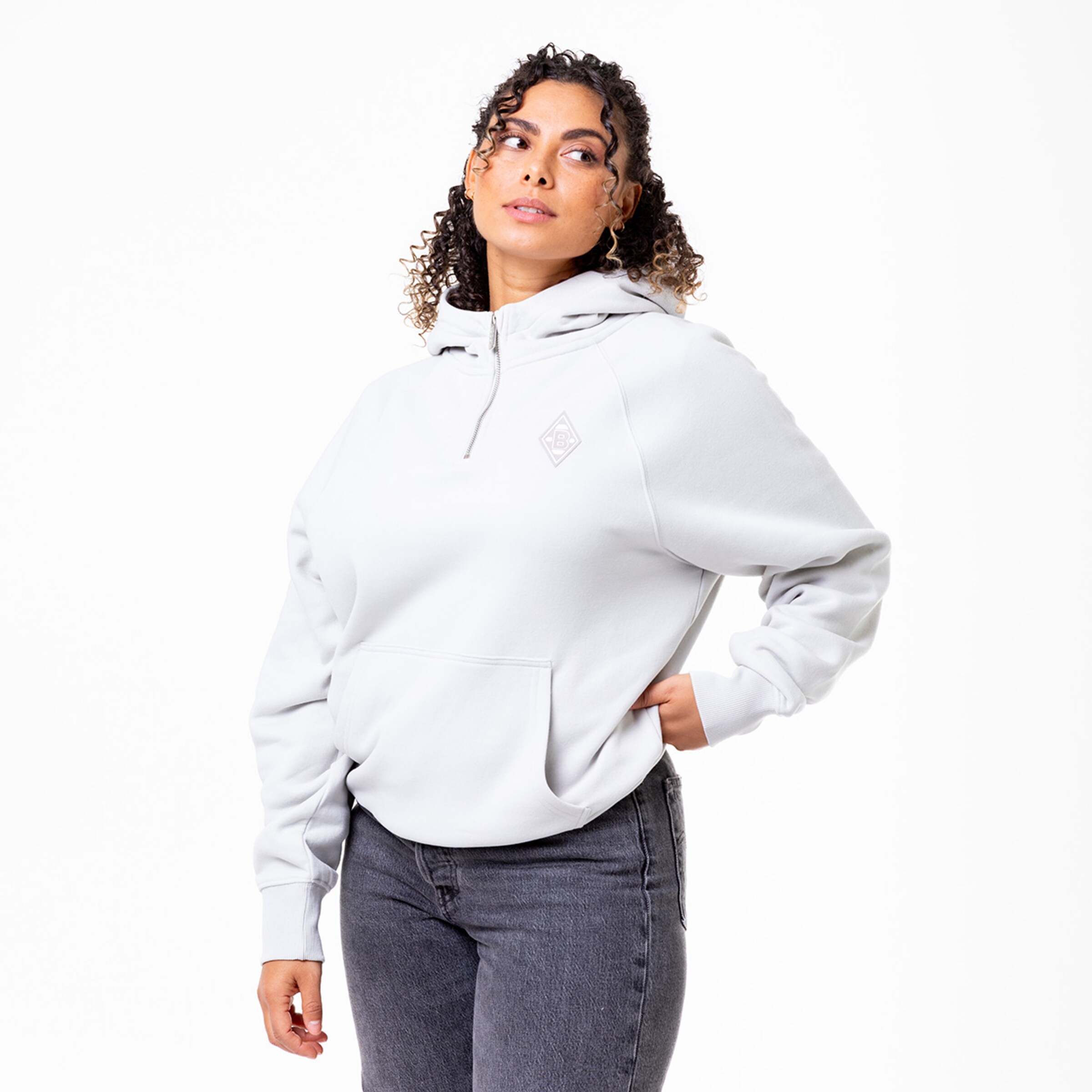 Frau mit lockigem Haar trägt einen grauen Kapuzenpullover und Jeans.