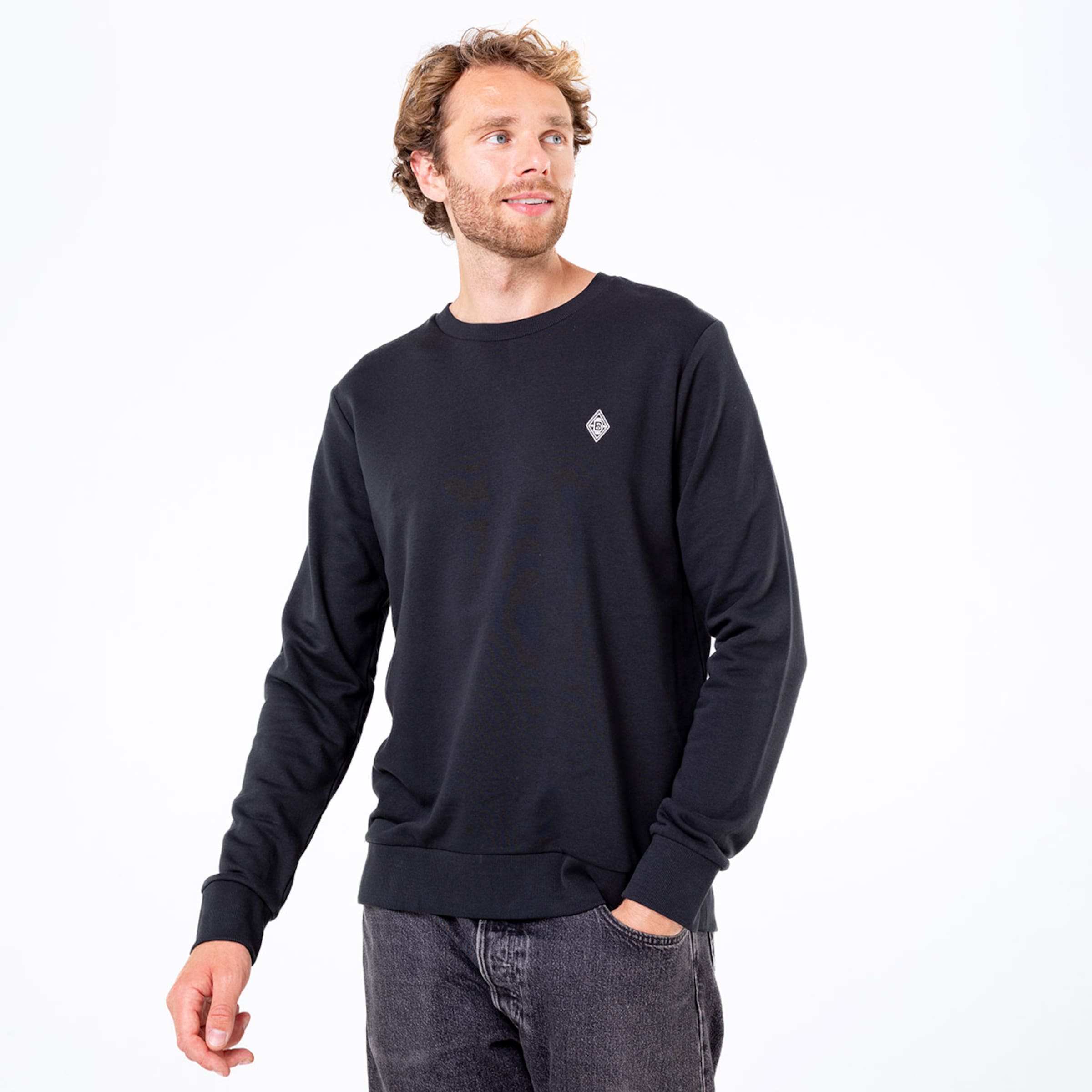 Mann in schwarzem Sweatshirt mit Logo auf der Brust und lässiger Pose.