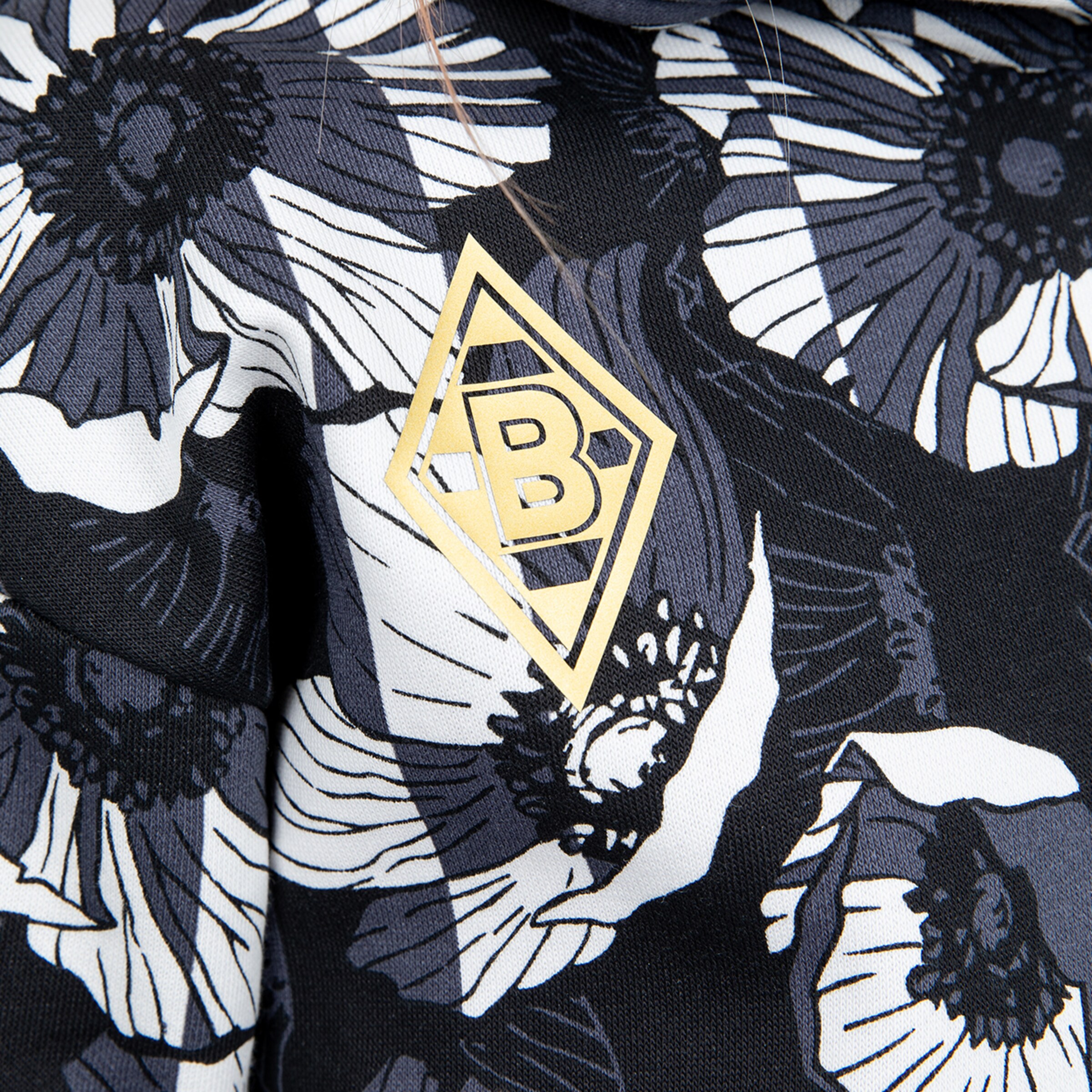 Close-up of fabric featuring a large floral pattern with the Borussia Mönchengladbach logo in gold.