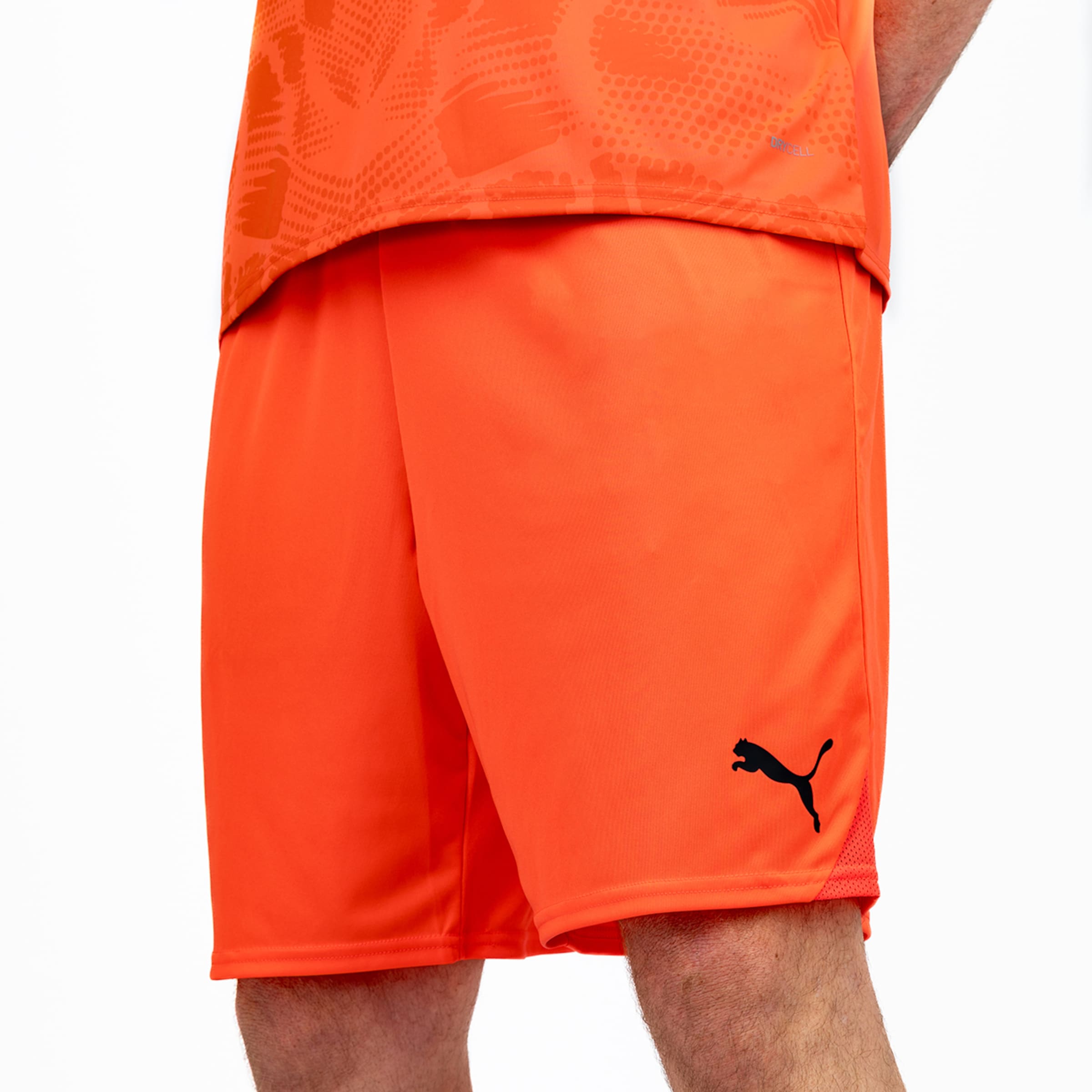 Nahaufnahme einer orangefarbenen Puma Sportshorts mit schwarzem Logo, kombiniert mit einem passenden gemusterten Trikot.