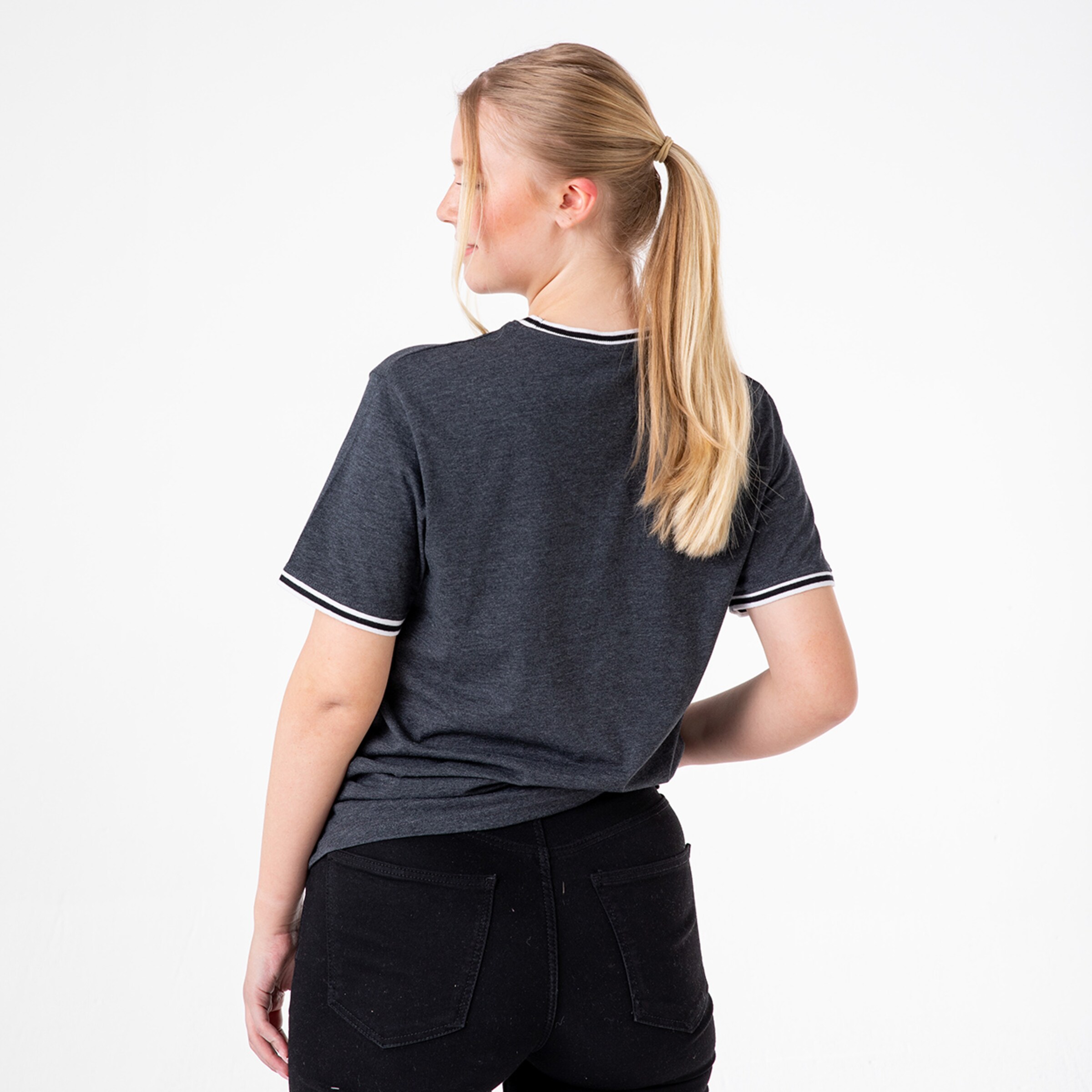 Junge Frau mit blonden Haaren trägt ein graues T-Shirt mit weißen Details von hinten gesehen.