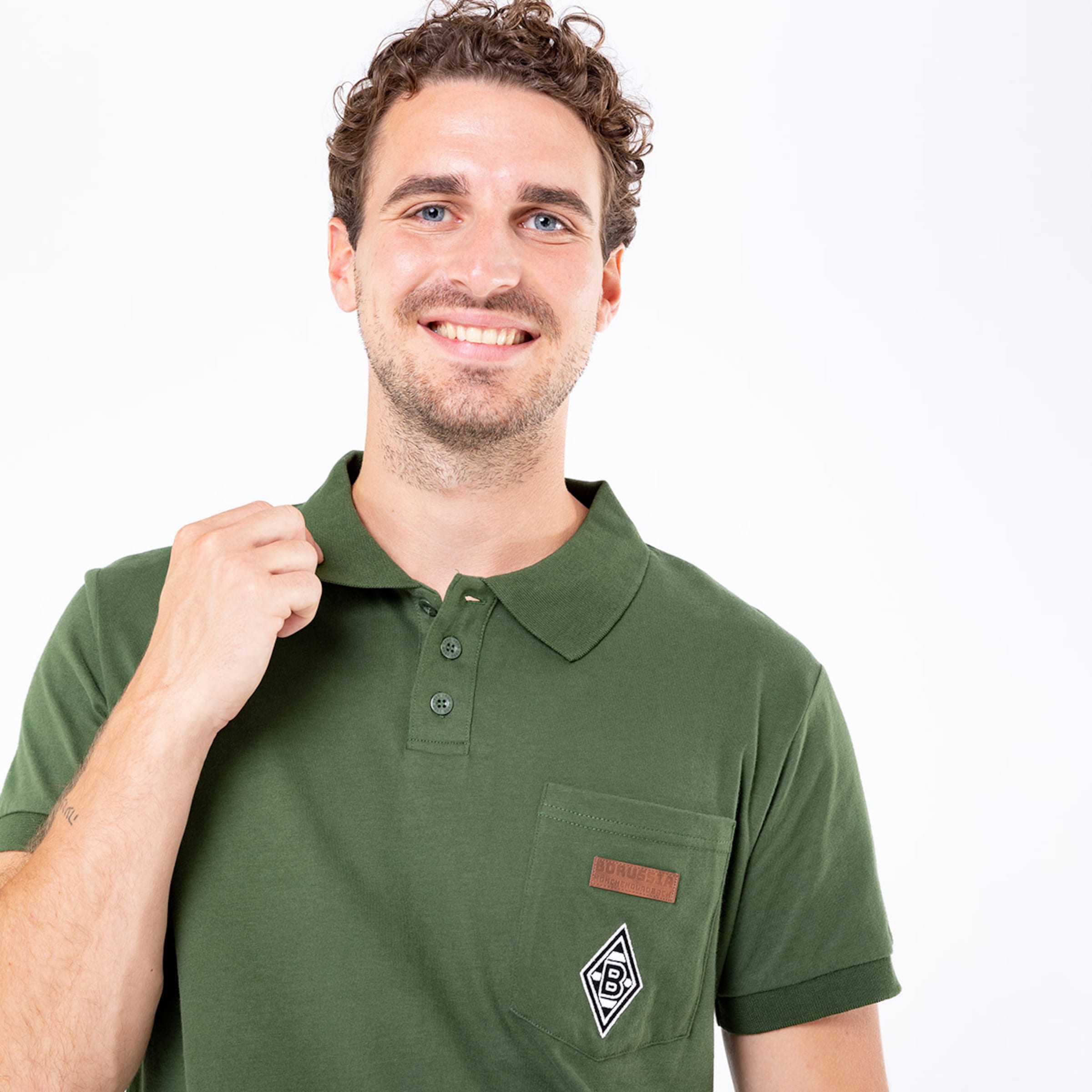 Man with curly hair wearing a green polo shirt featuring Borussia Mönchengladbach logo.