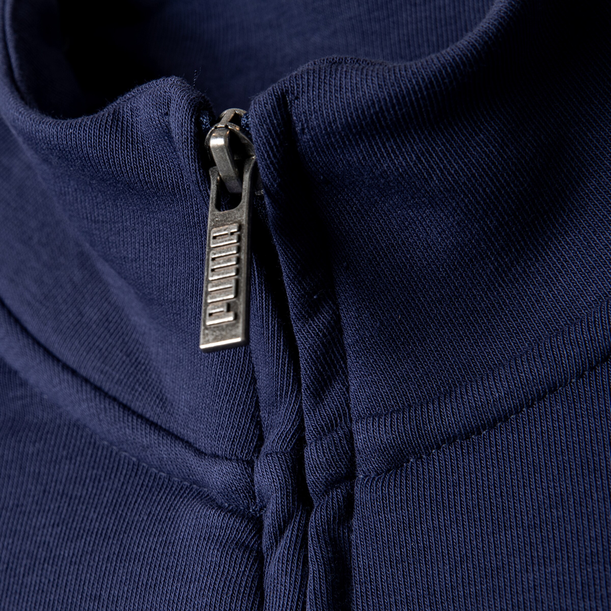 Nahaufnahme eines schwarzen PUMA-Reißverschlusses an einem Sportoberteil.