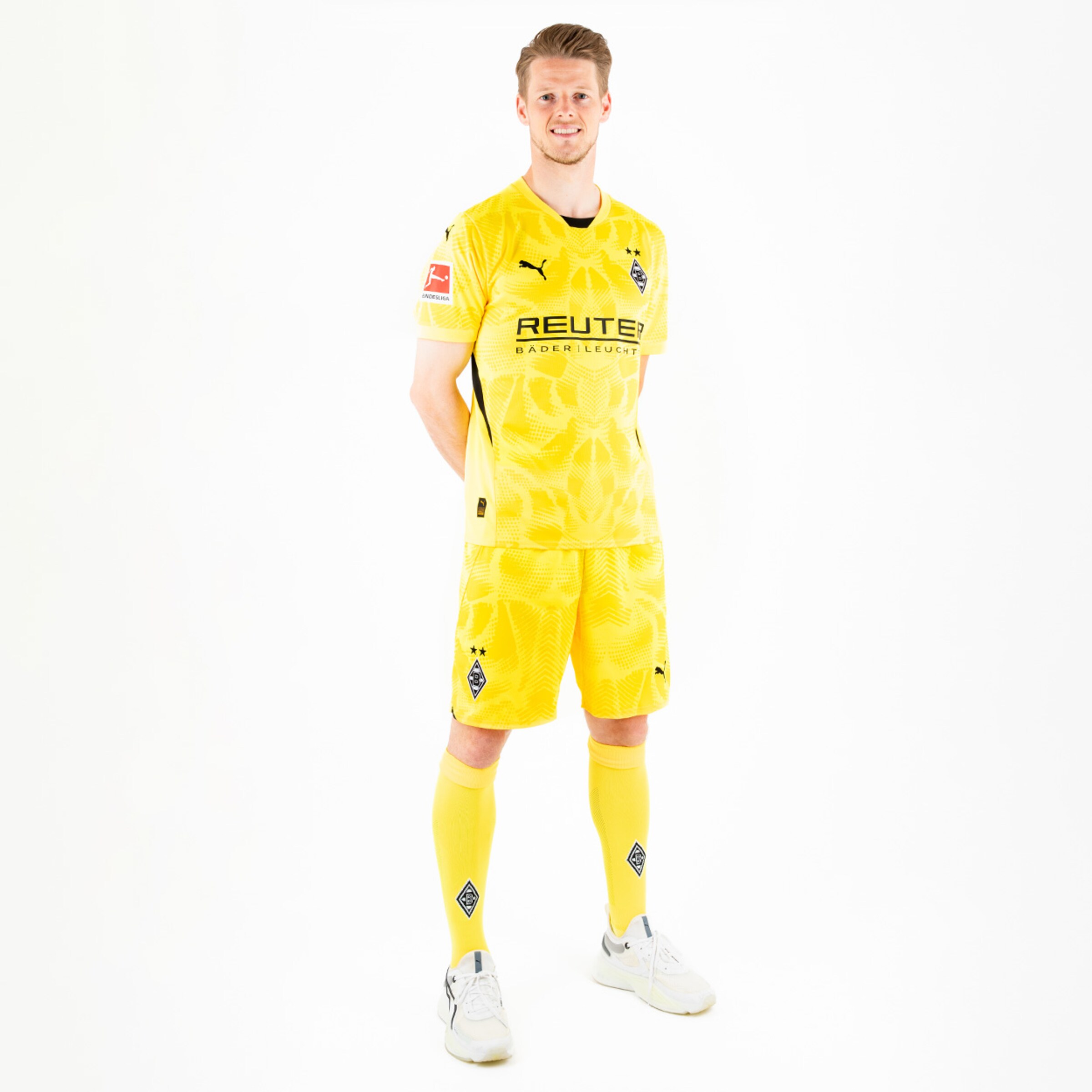 Spieler im gelben Borussia Mönchengladbach Trikot steht aufrecht mit Händen hinter dem Rücken.