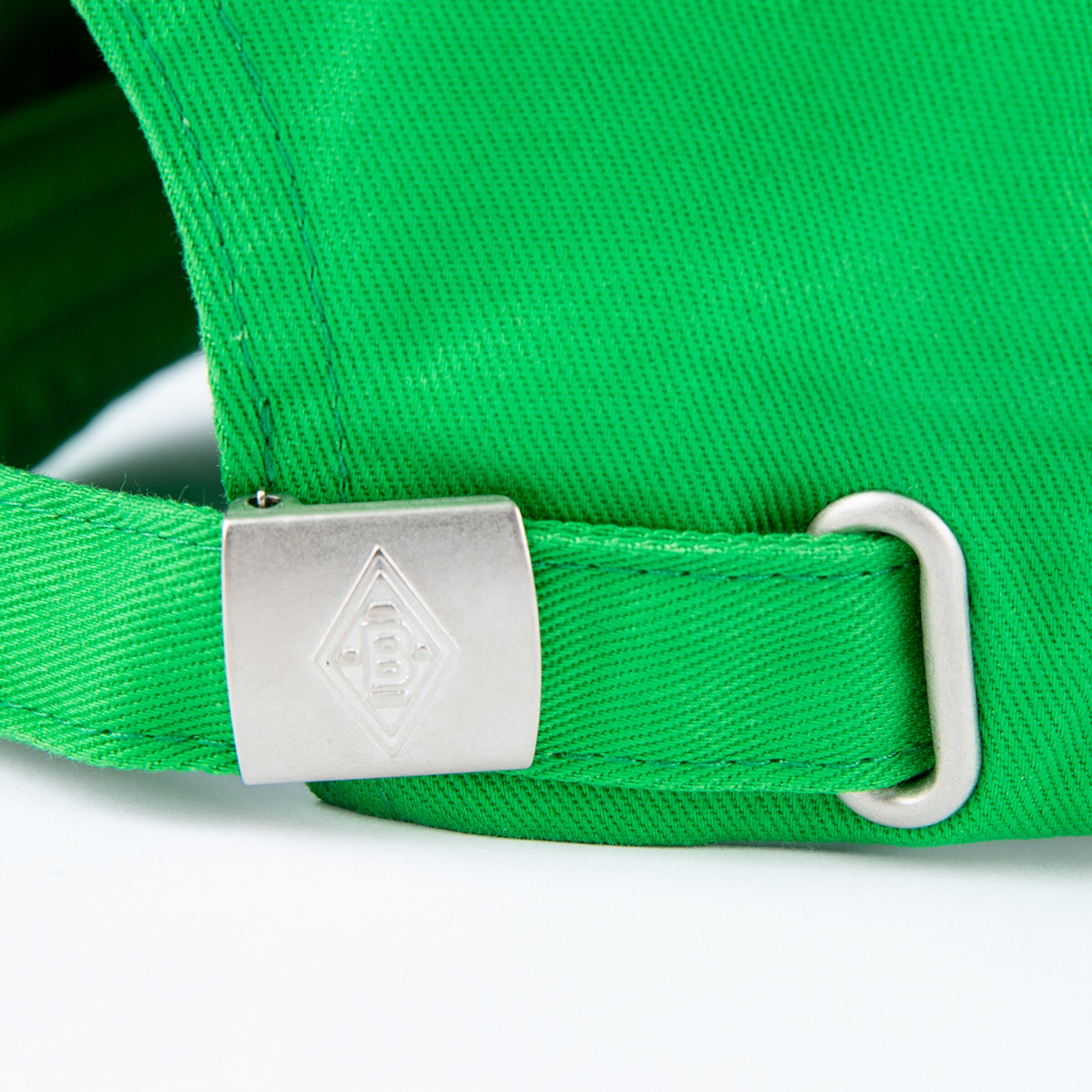 Detailansicht einer grünen Mütze mit einem verstellbaren Riemen und einem metallischen Logo-Clip.