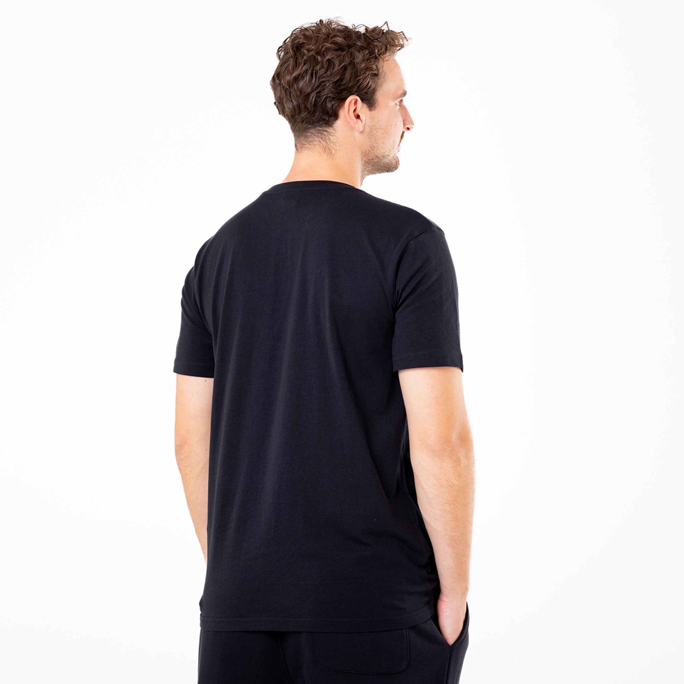 Mann mit kurzen Ärmeln der von hinten steht trägt ein schwarzes T-Shirt und schaut zur Seite.